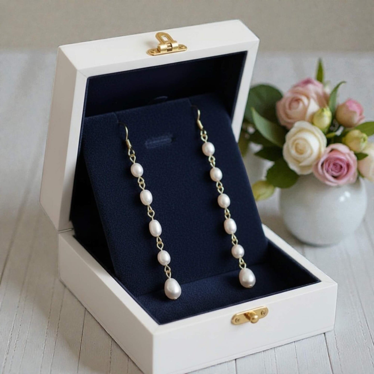Pearl necklace in a white jewelry box with a vase of flowers in the background