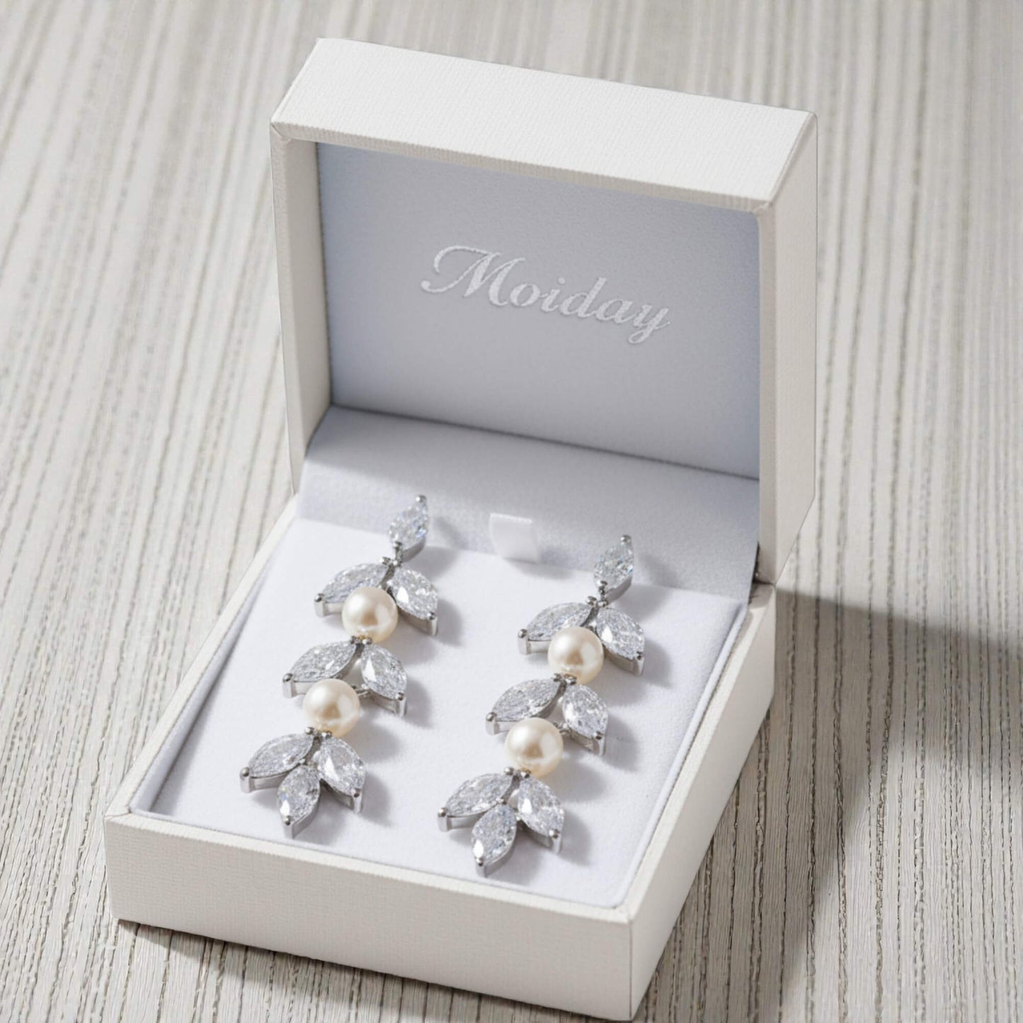 Pair of pearl and crystal earrings in a Moily branded box on a textured surface