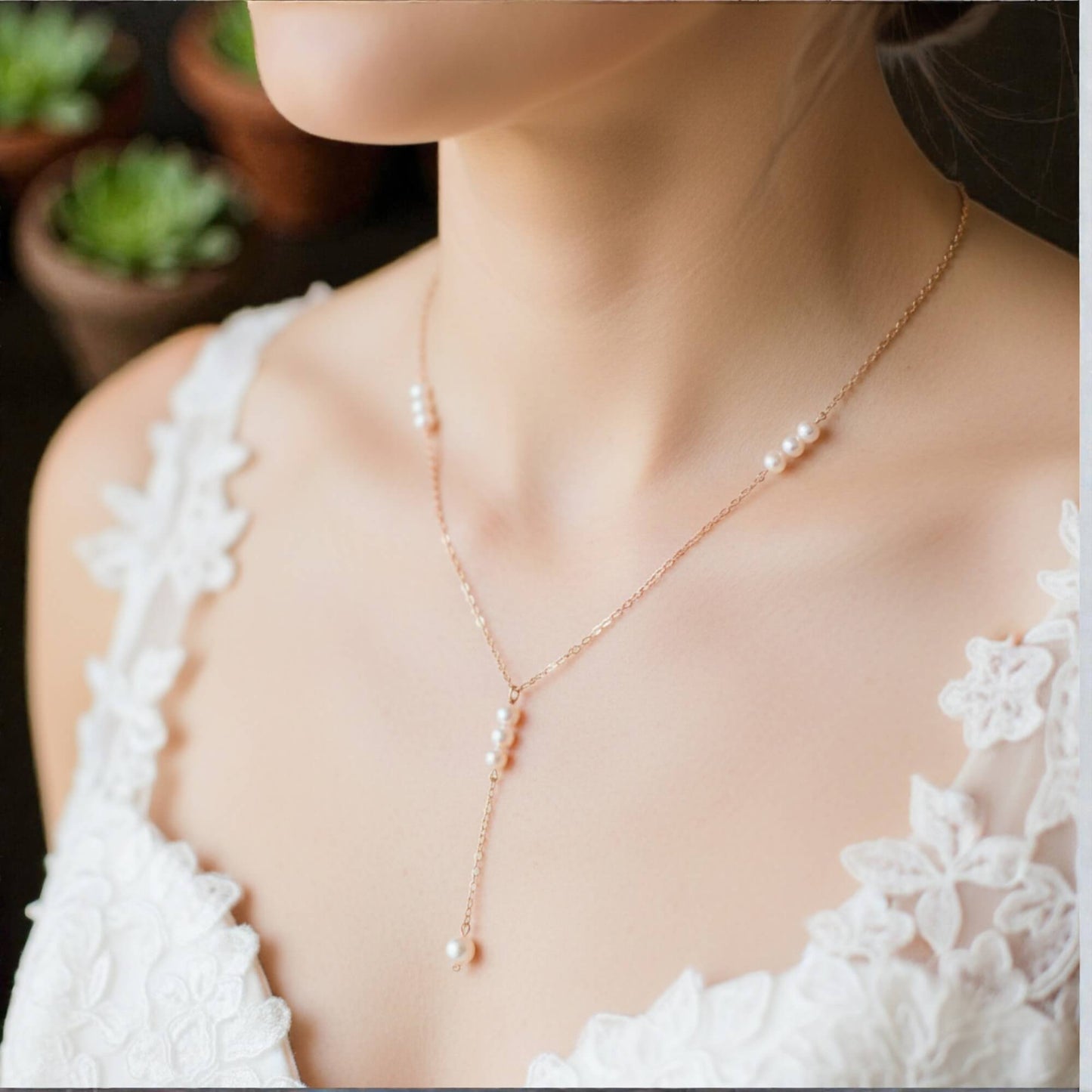 Pearl necklace worn by a person in a white lace top with a blurred background of potted plants.