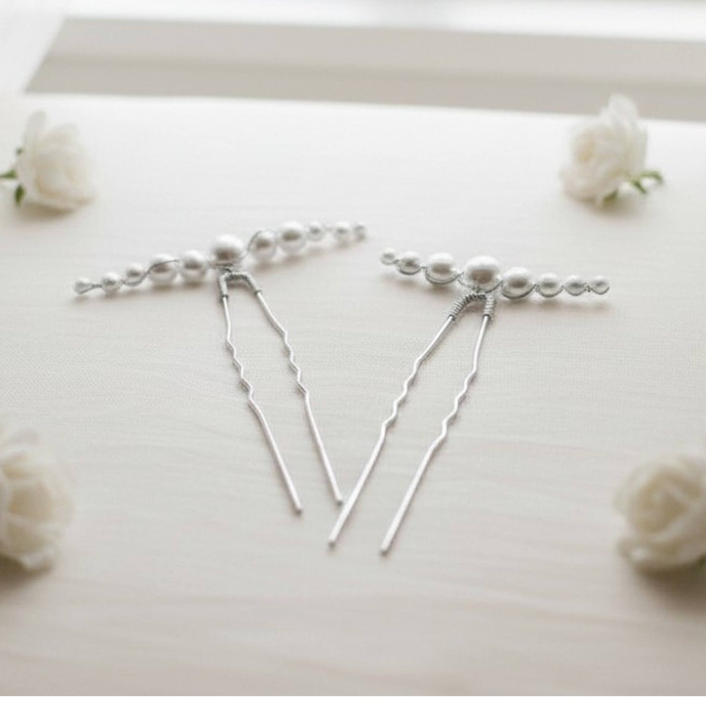 Silver hairpins with pearls on a white surface with small white flowers.