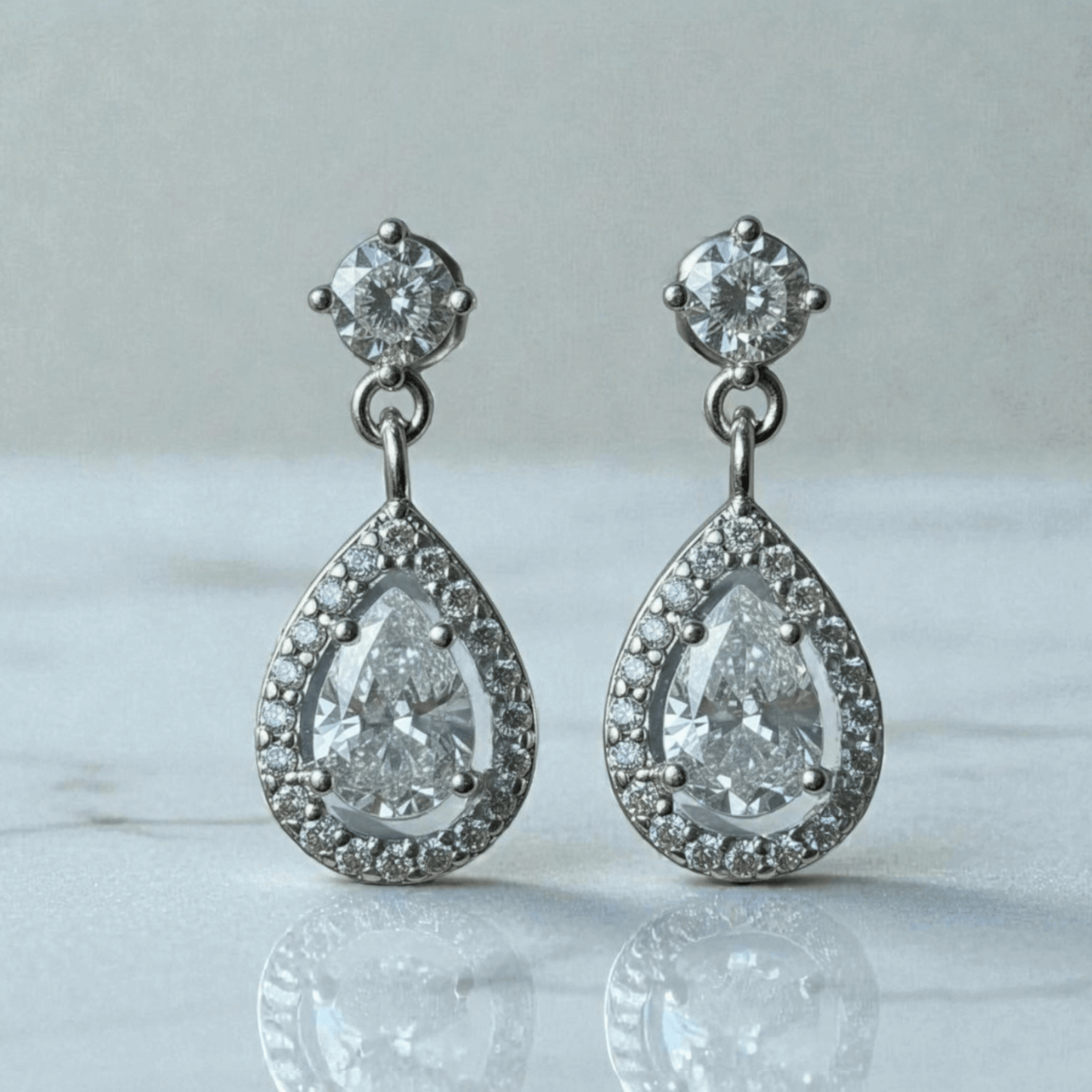 Teardrop-shaped silver earrings with clear gemstones on a marble surface.