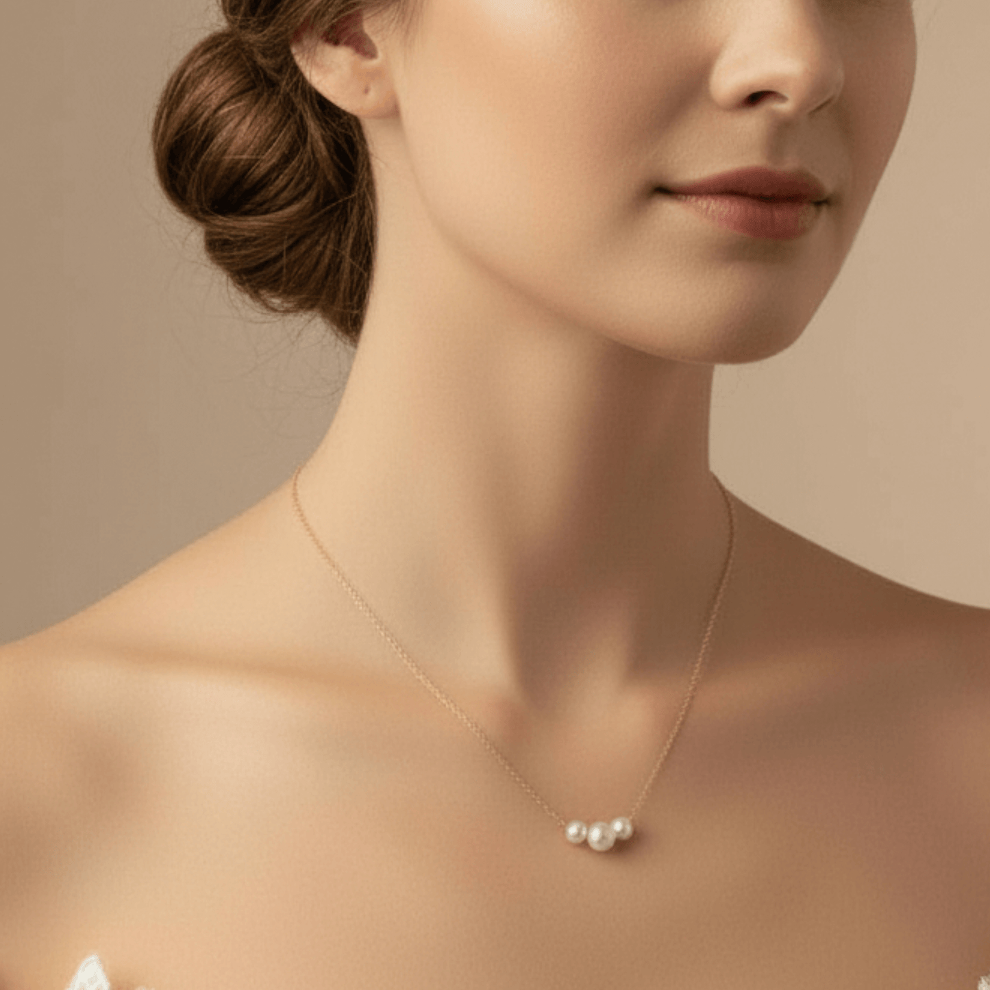 Woman wearing a delicate necklace with three pearls against a neutral background