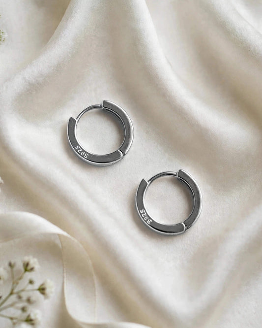 A pair of silver-toned 925 sterling silver half-hoop earrings resting on a draped cream satin fabric background.