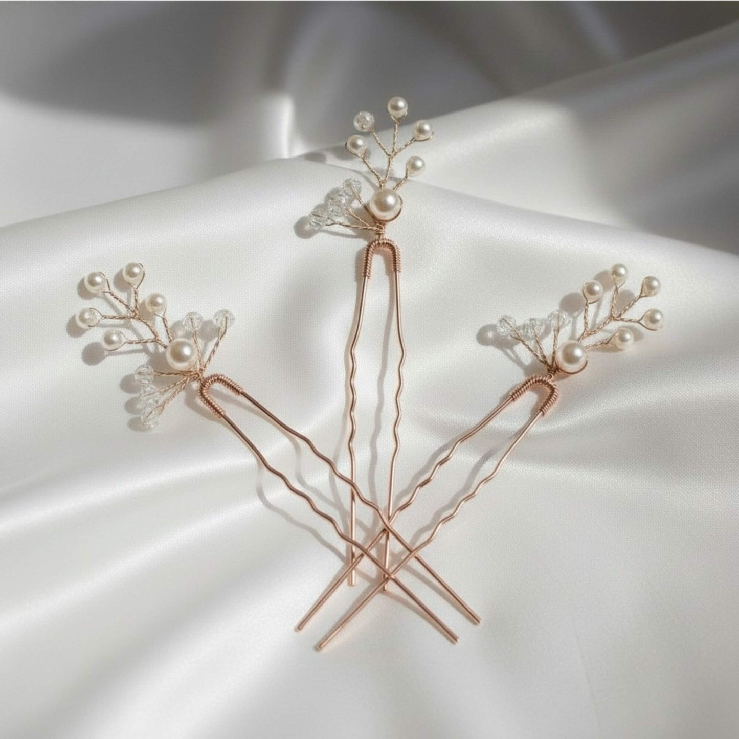Three rose gold bridal hair pins with pearl and crystal branches arranged on soft white fabric.