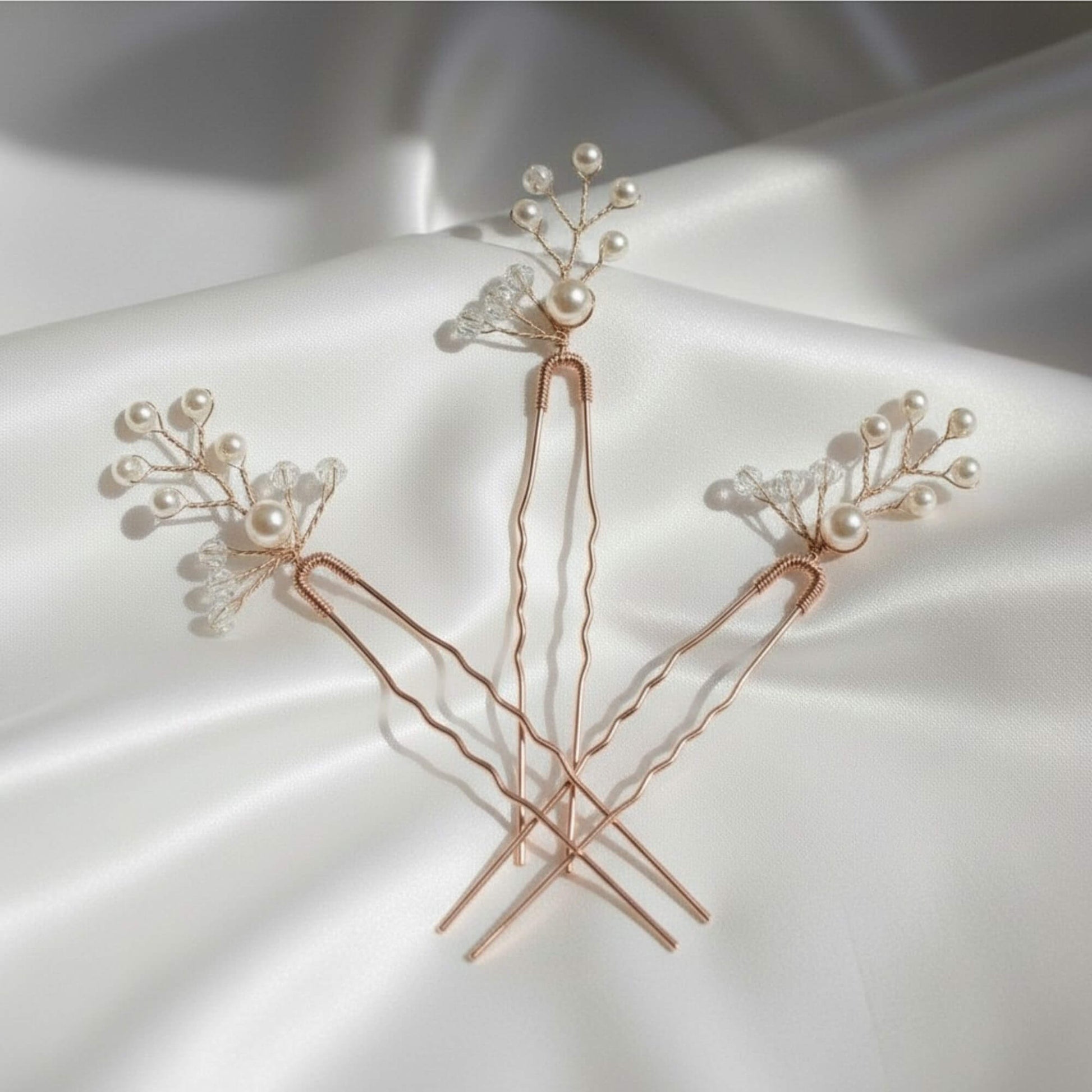 Three rose gold bridal hair pins with pearl and crystal branches arranged on soft white fabric.
