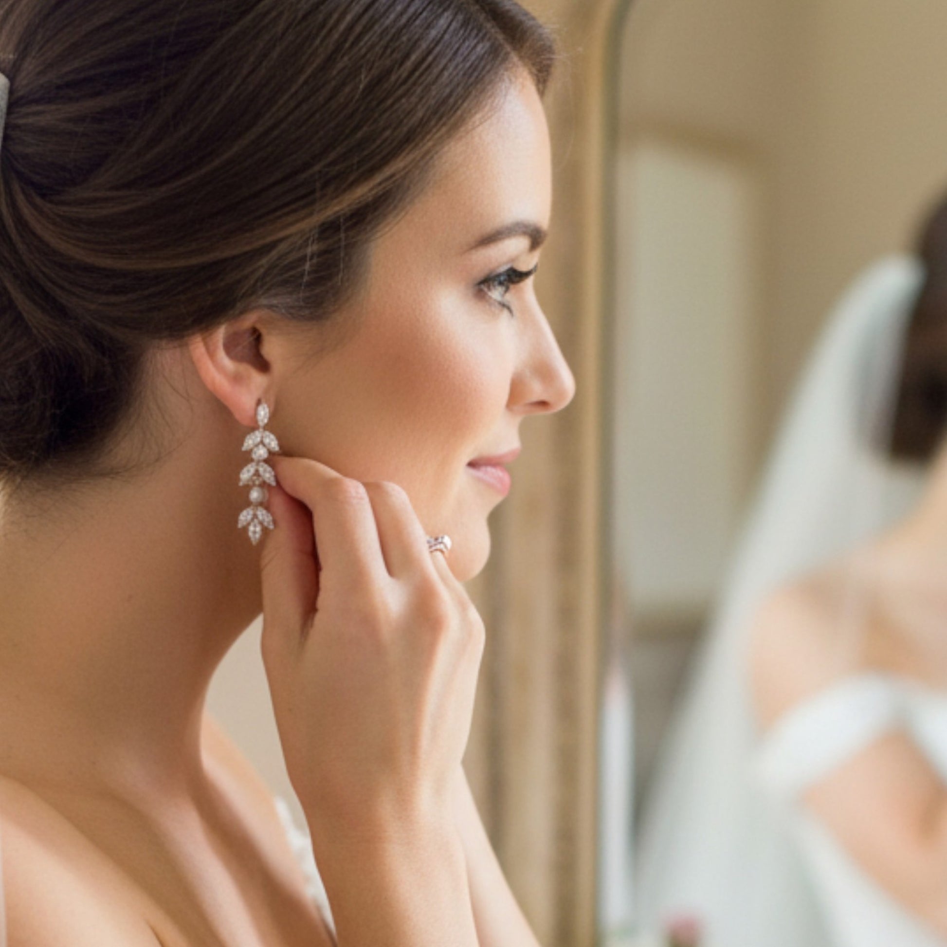 Bride in soft warm lighting wearing pearl drop earrings with marquise crystals, minimal bridal styling.