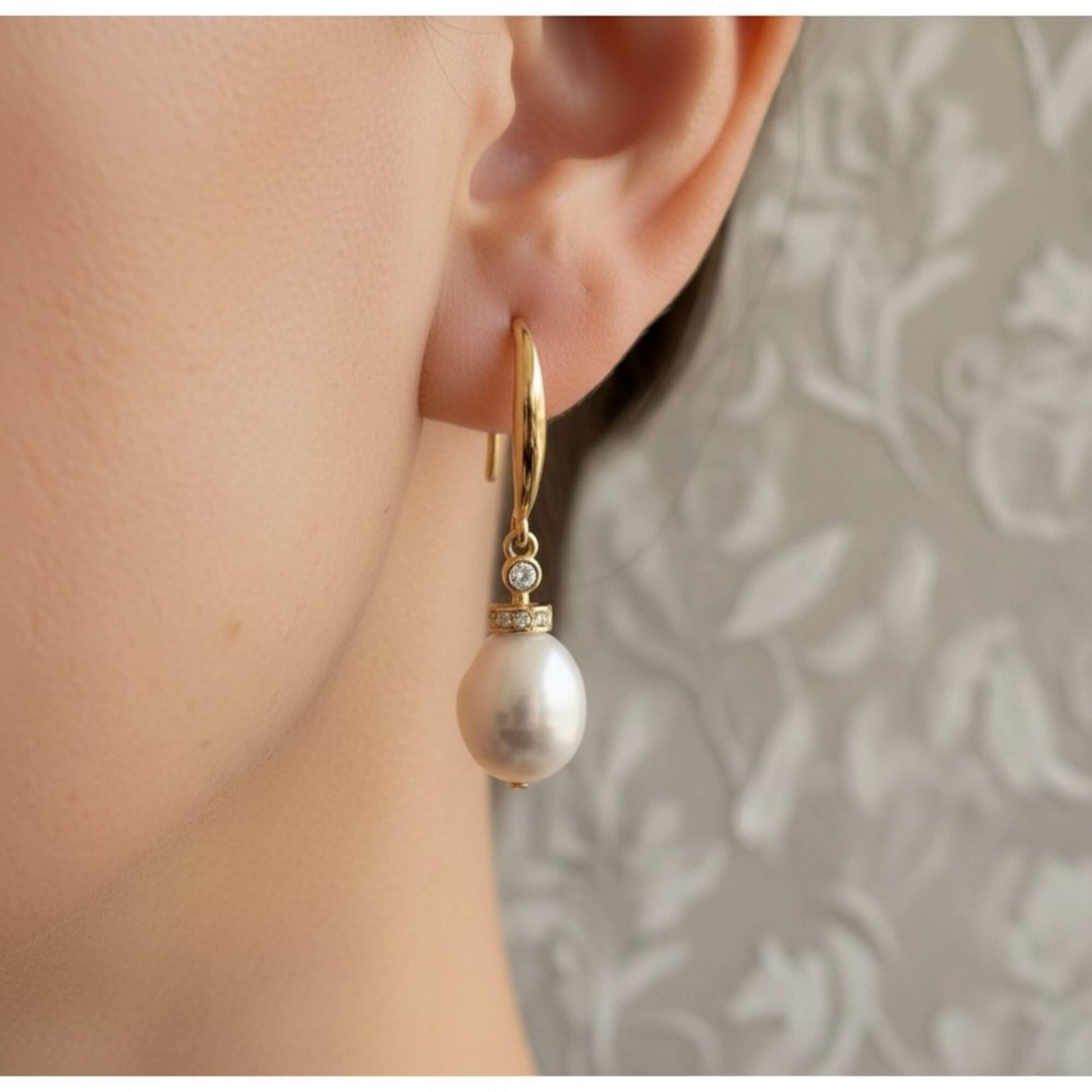 Close-up of bride wearing gold pearl drop earrings with zirconia accent, soft lighting and elegant bridal mood.