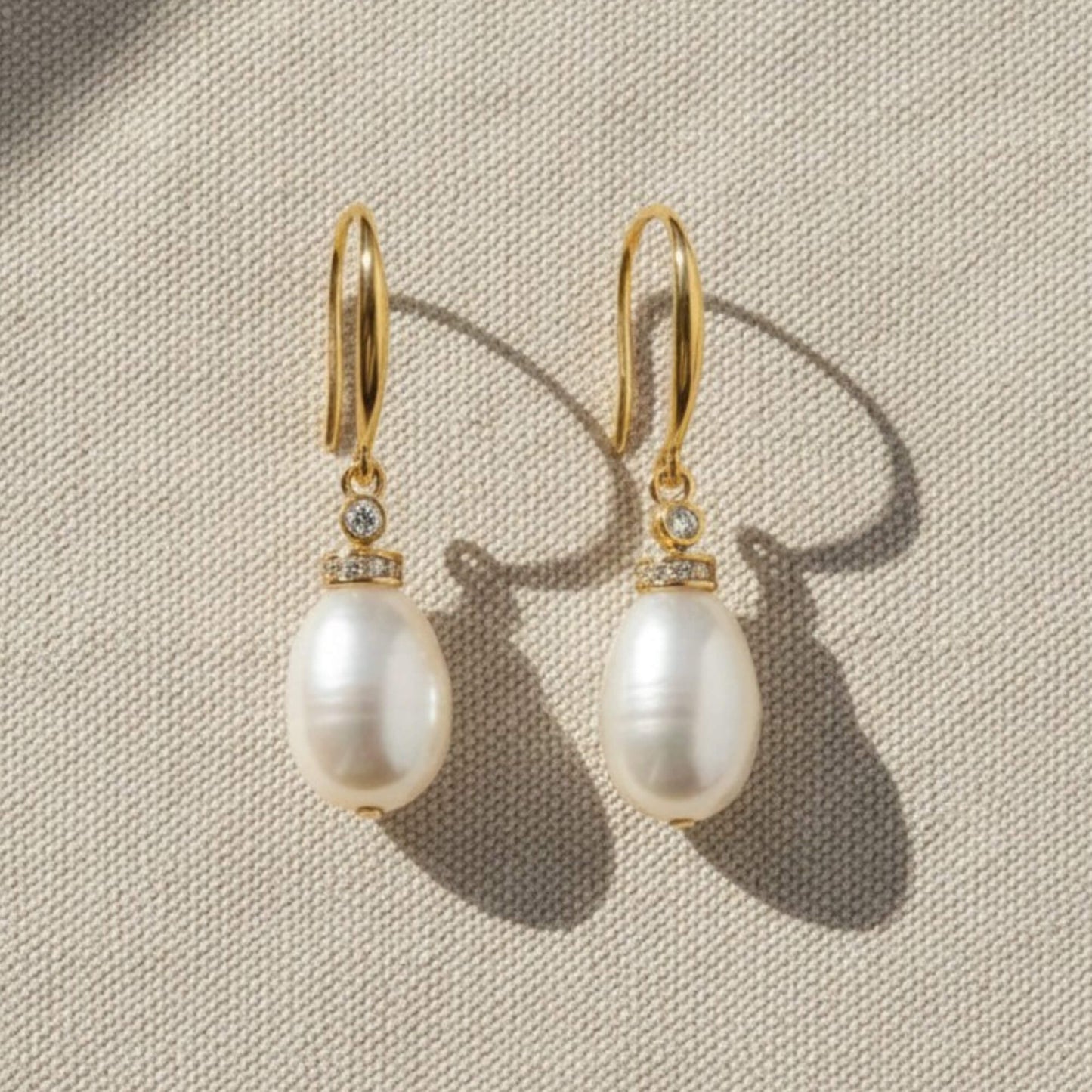 Close-up of gold pearl drop earrings with zirconia accent on white fabric, elegant bridal jewellery.