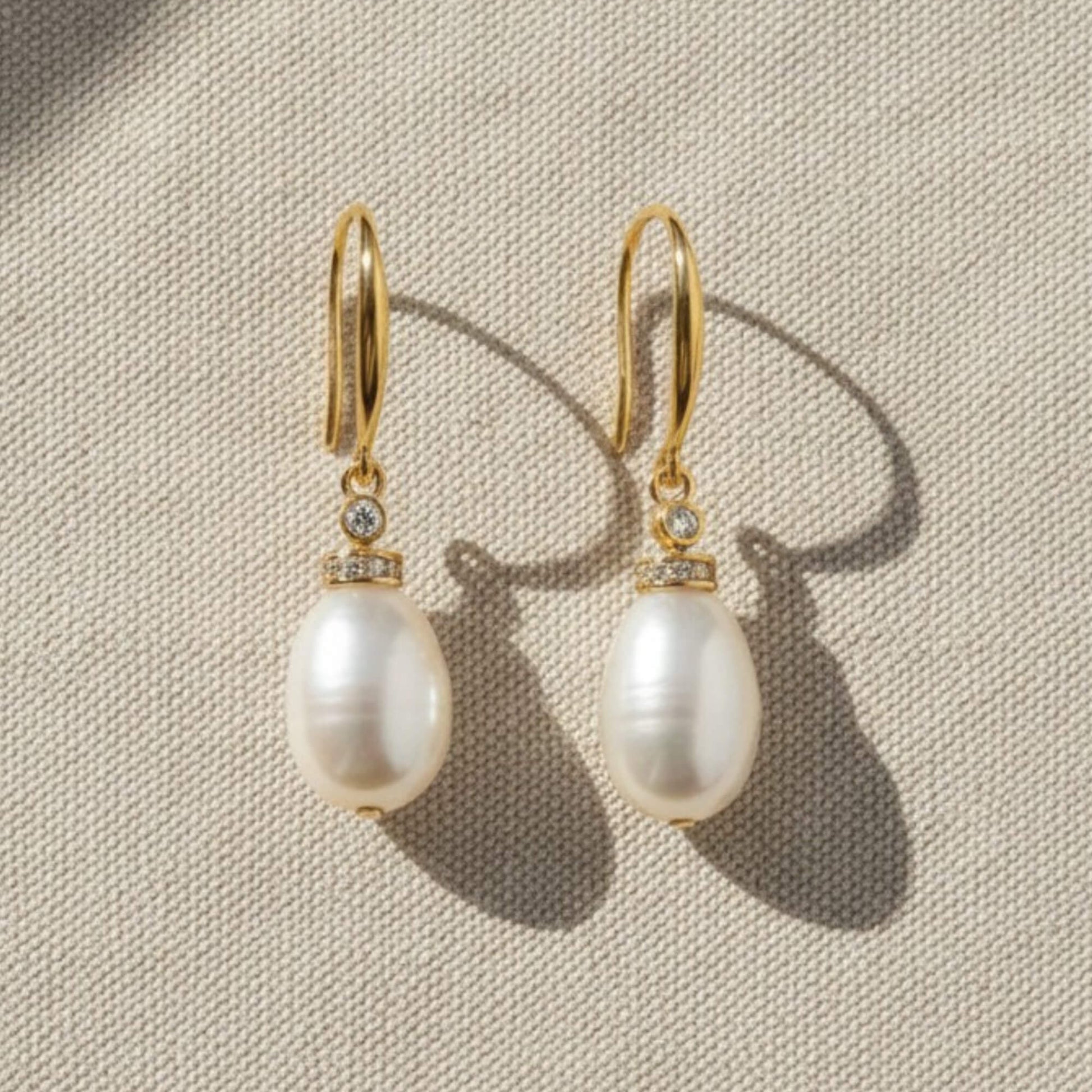Close-up of gold pearl drop earrings with zirconia accent on white fabric, elegant bridal jewellery.