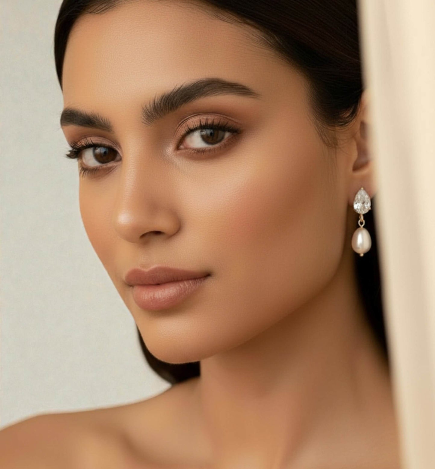 Close-up of a woman wearing pearl earrings with a neutral background