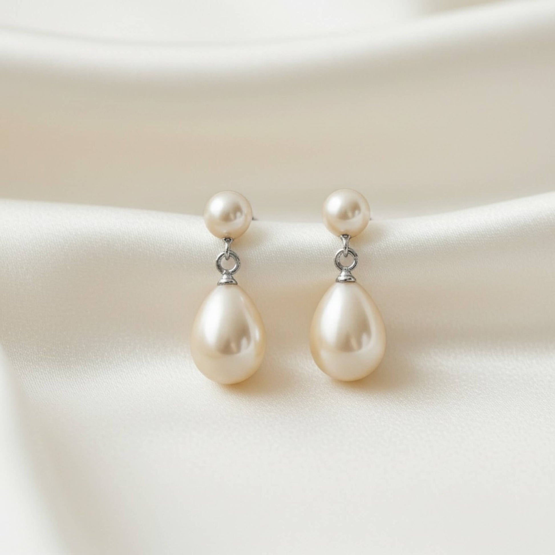 Matching pearl drop earrings and necklace laid on smooth satin fabric, premium bridal jewellery with soft highlights.