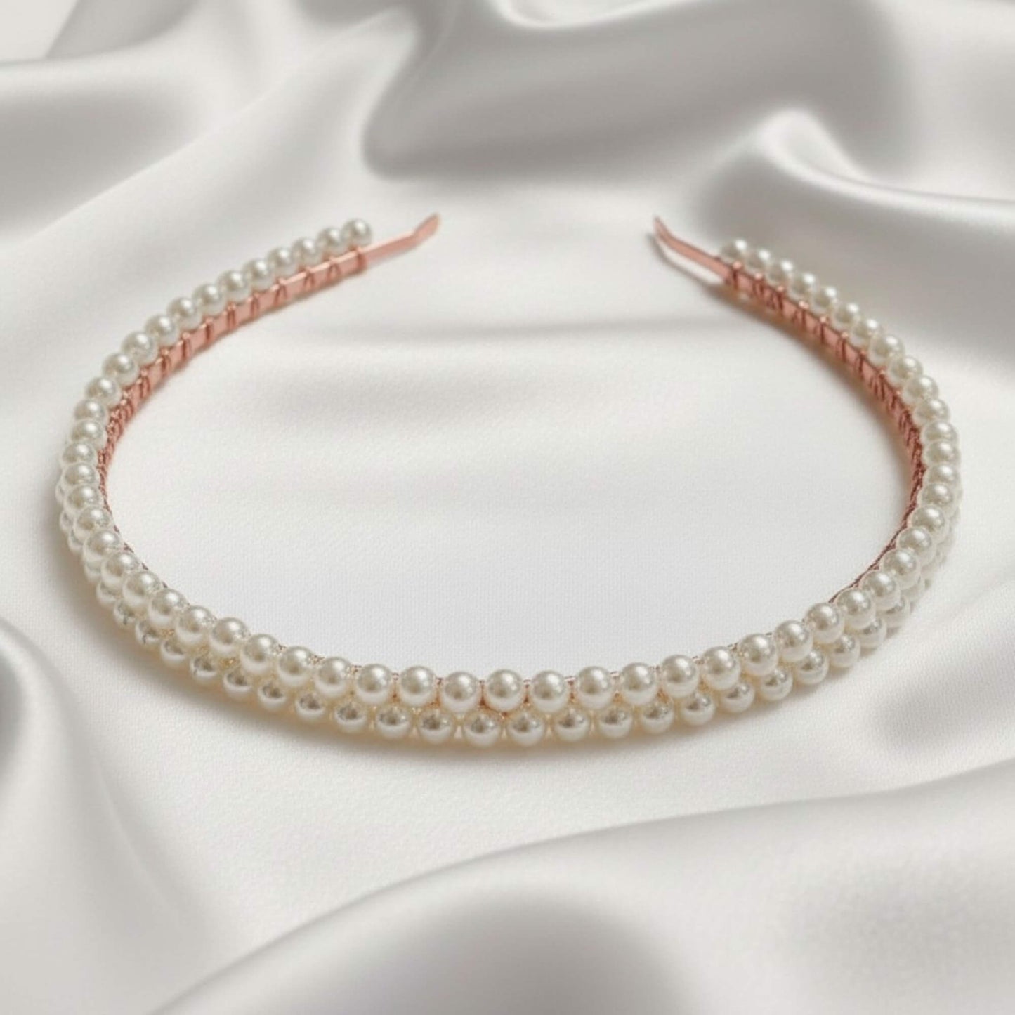 Elegant bridal headband with soft‑white glass pearls resting on white satin fabric.