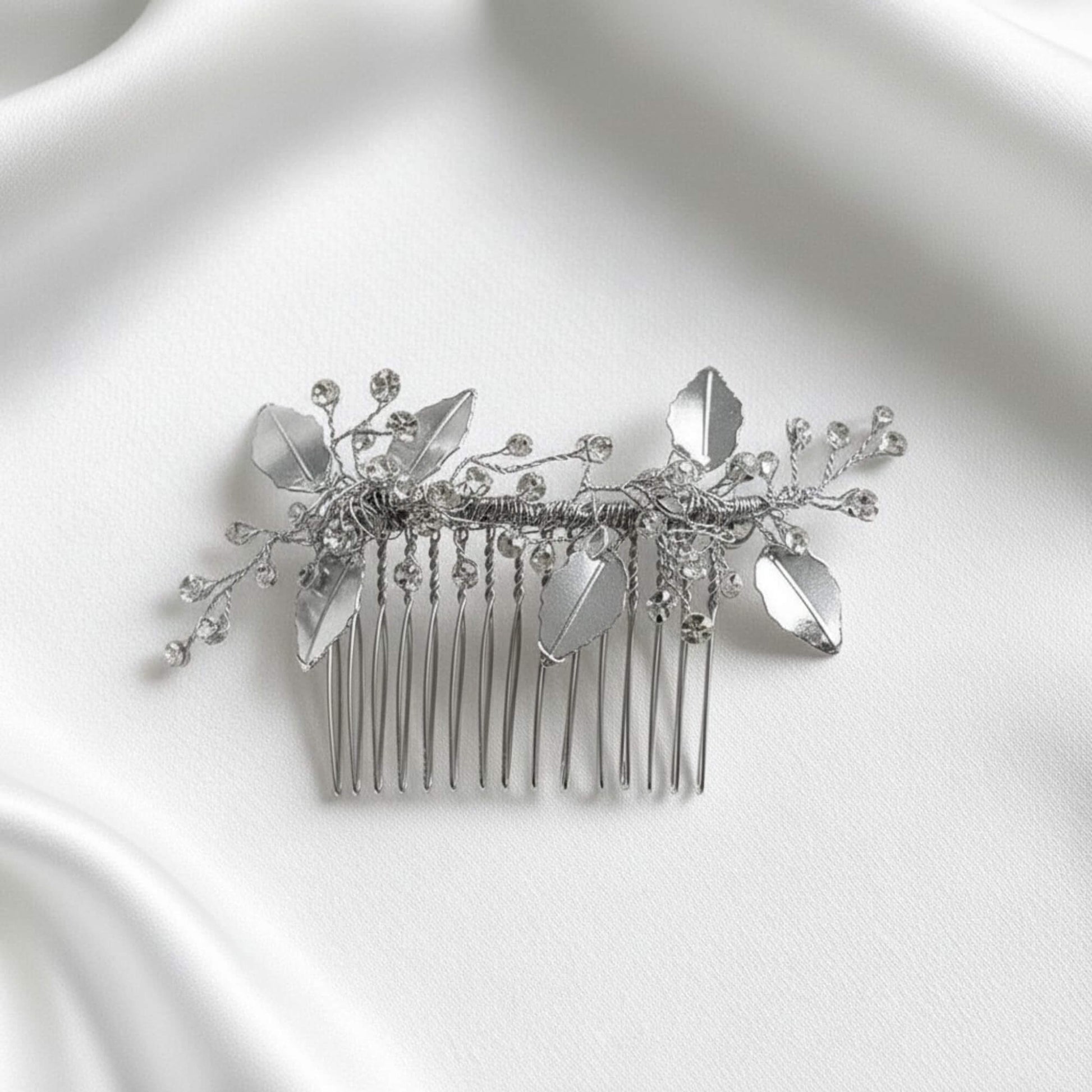 Silver botanical hairpiece lit by natural window light on stone surface.