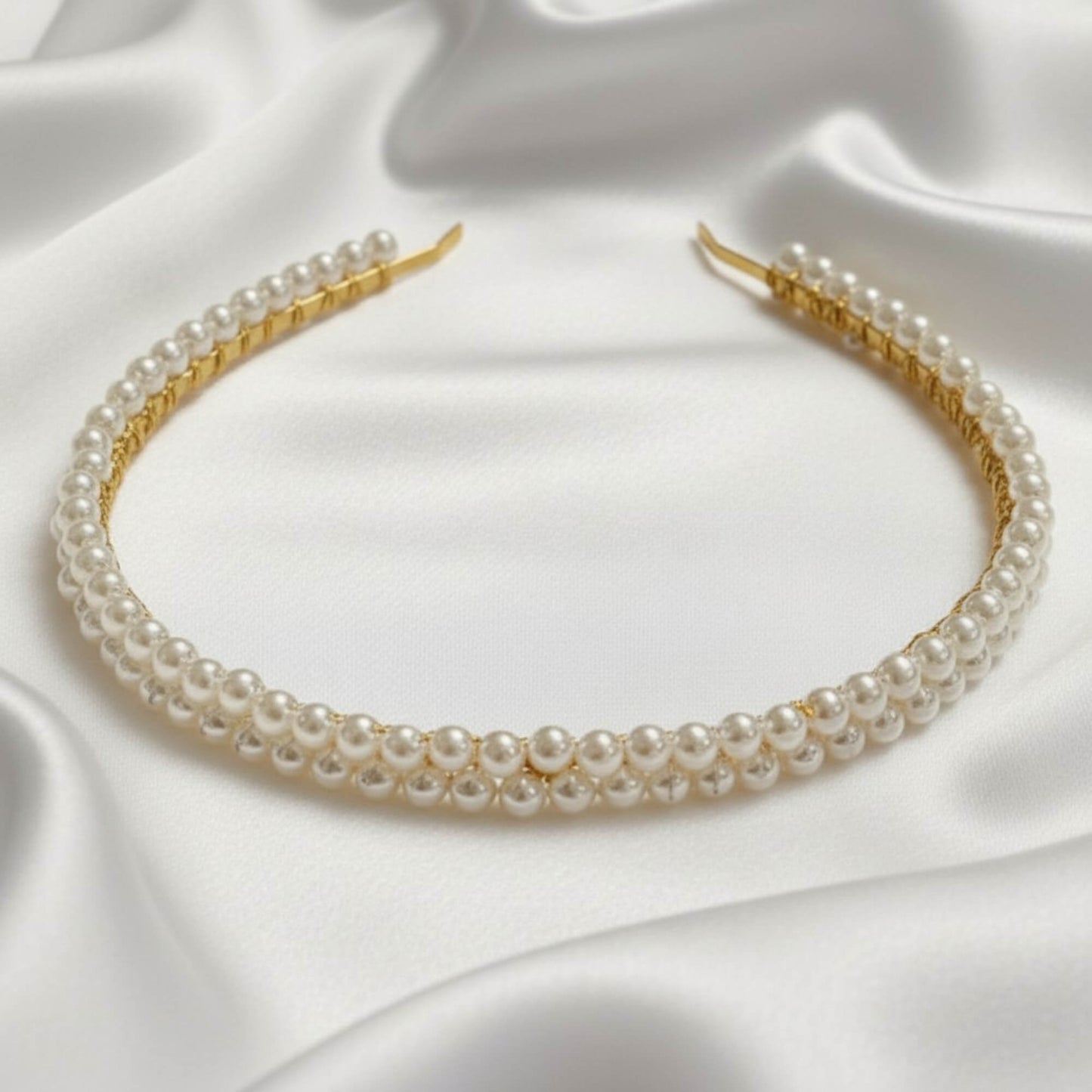 Bridal headband with double rows of soft‑white glass pearls on a gold base, photographed on white satin.