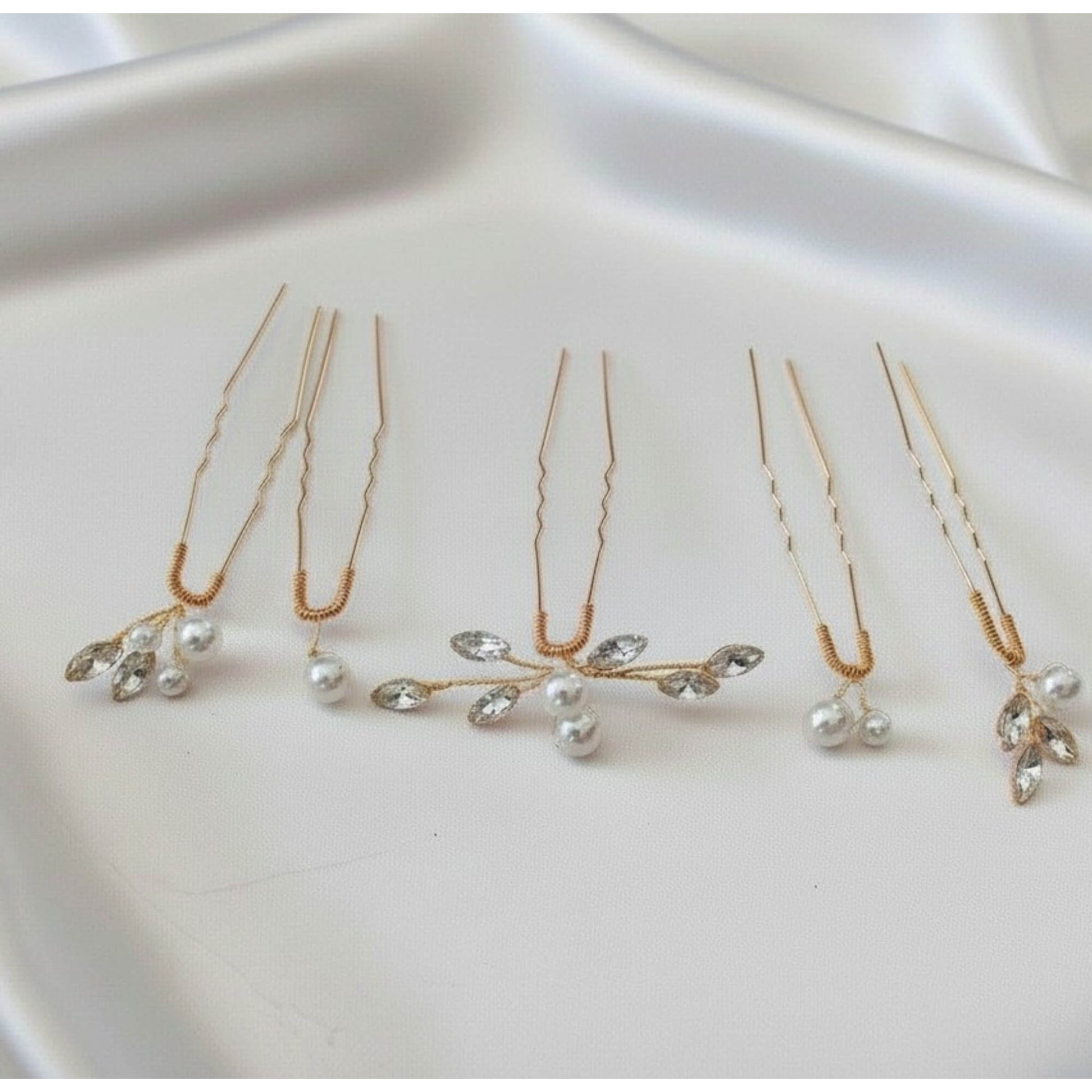 Rose gold pearl and crystal wedding hair pins arranged on soft satin fabric.