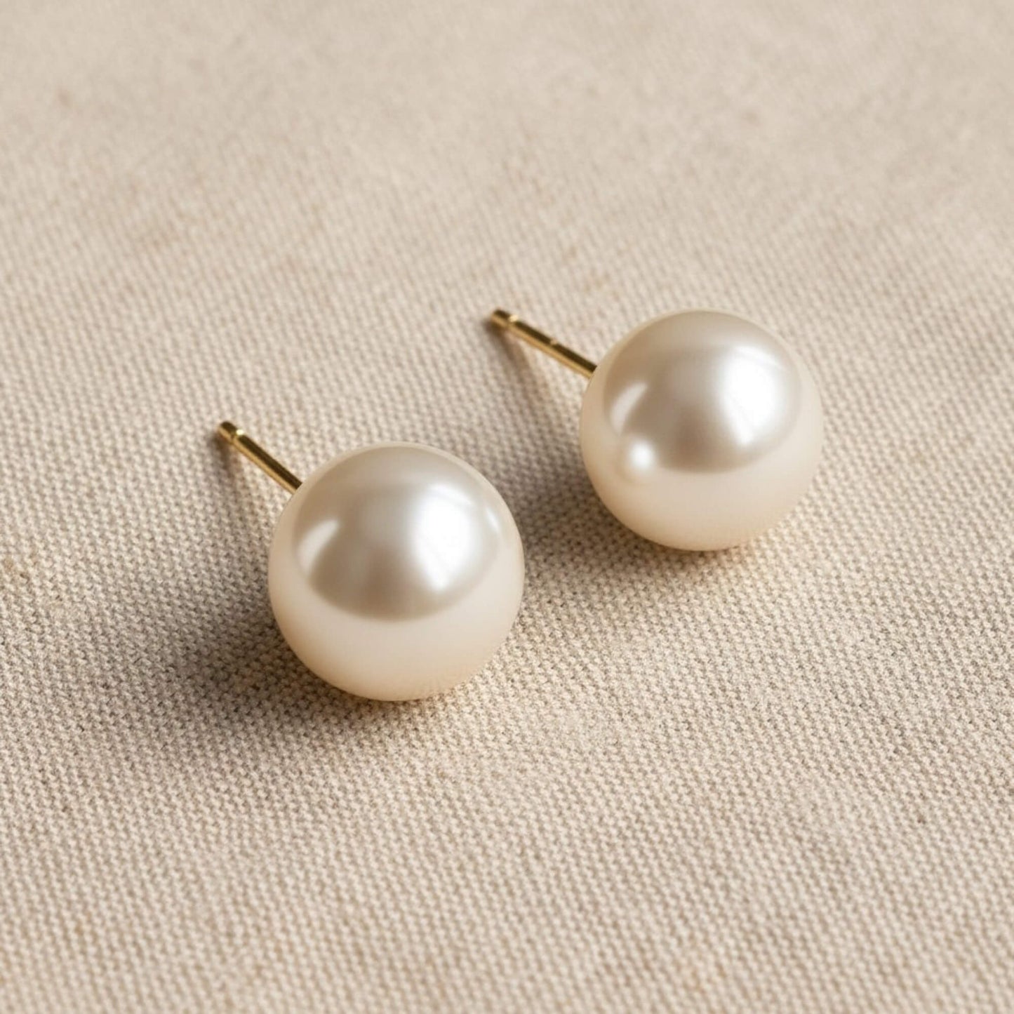 Pair of pearl earrings on a beige fabric background