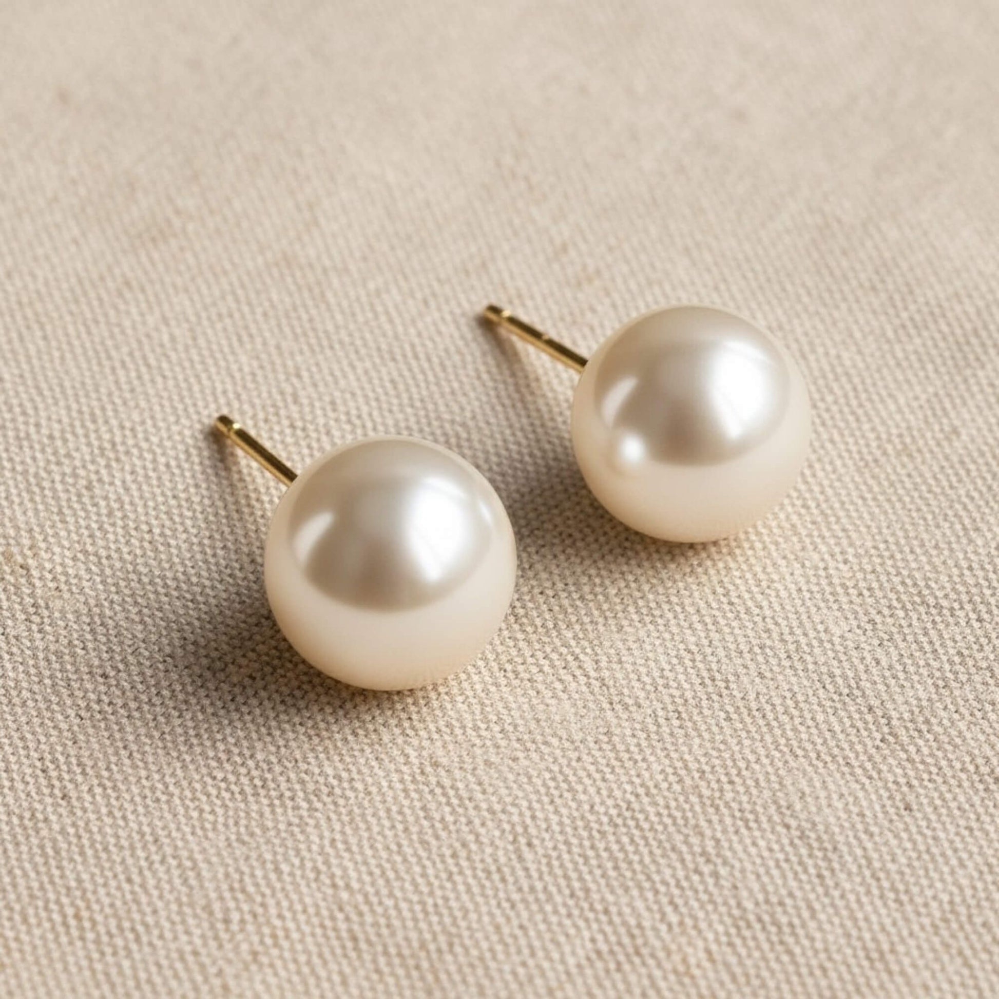 Pair of pearl earrings on a beige fabric background
