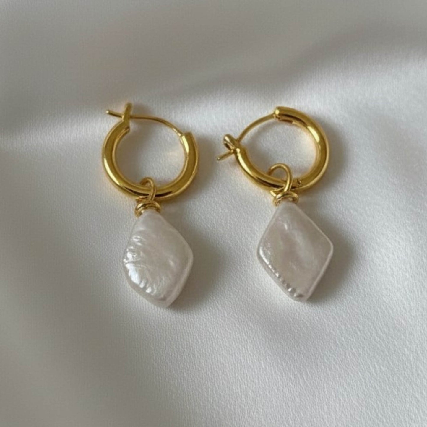 Close-up of silver hoop earrings with ivory geometric drop charm on white fabric, minimal modern jewellery.