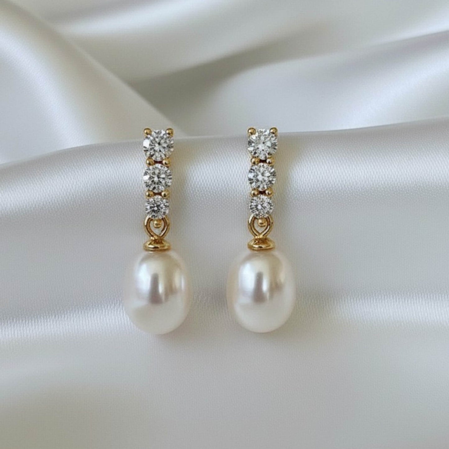 Close-up of gold hook earrings with white pearl drop and zirconia accent on white fabric, elegant bridal jewellery.