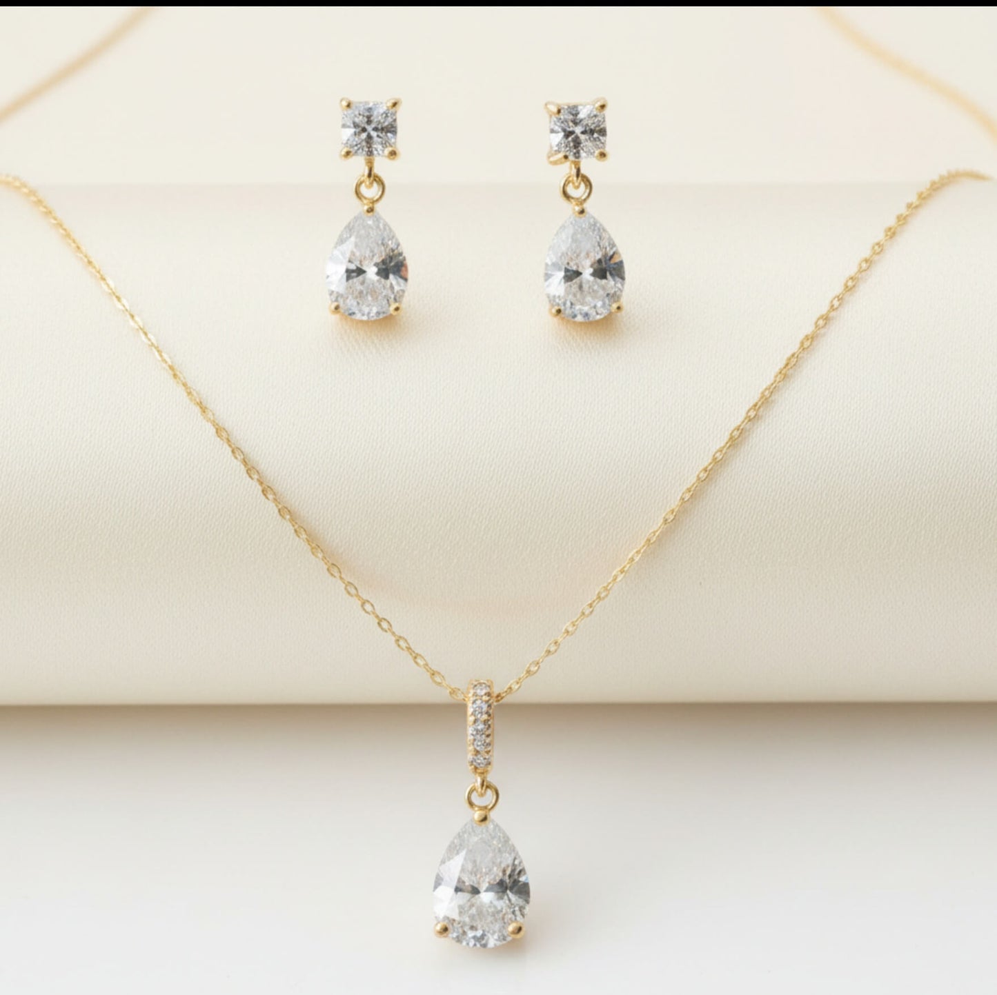 Gold necklace and earrings with clear gemstones on a beige background