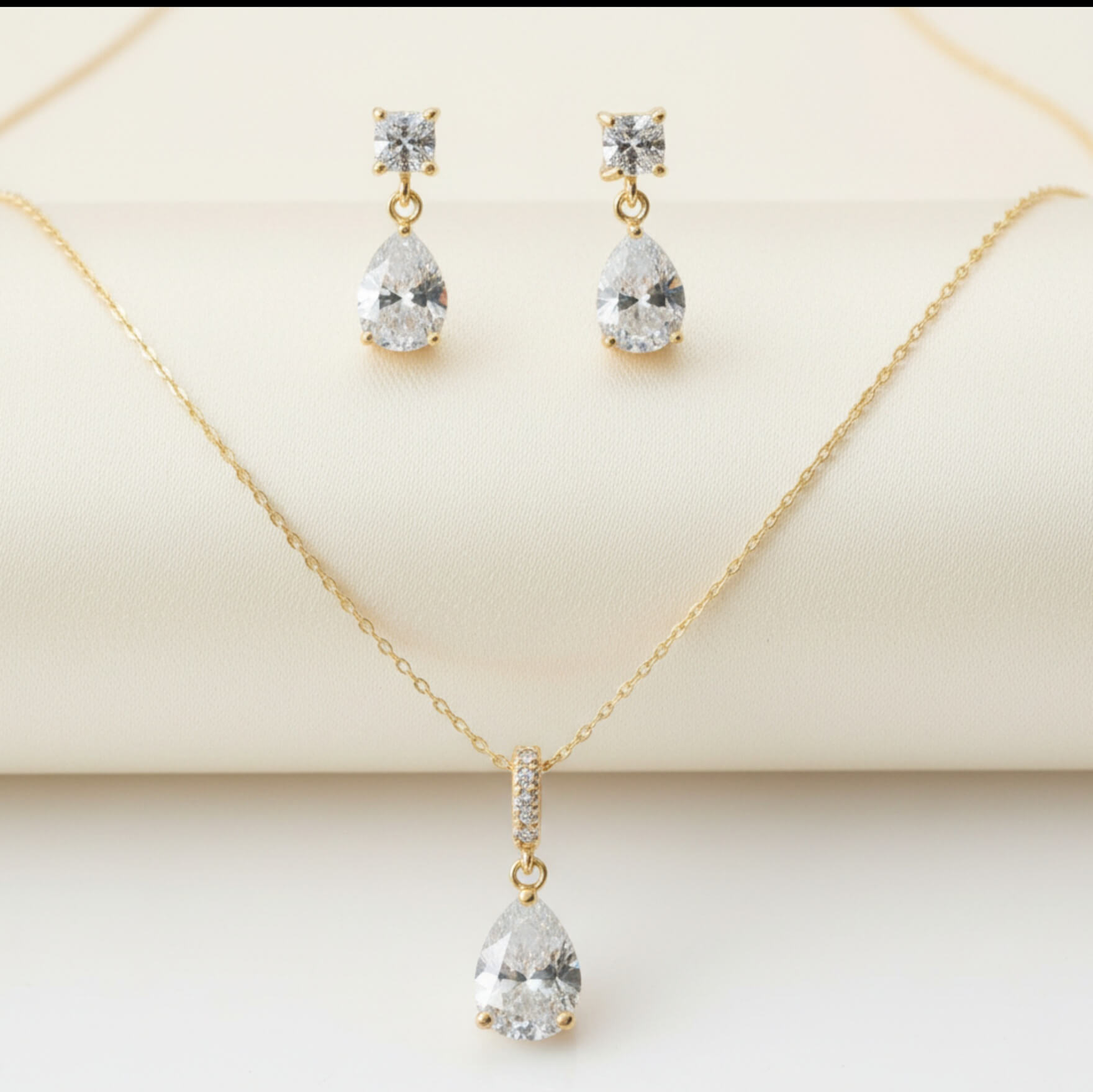 Gold necklace and earrings with clear gemstones on a beige background