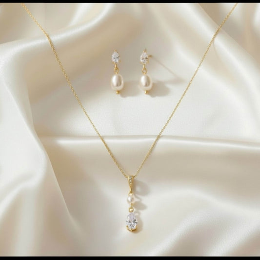 Gold necklace and earrings with pearl accents on a beige fabric background