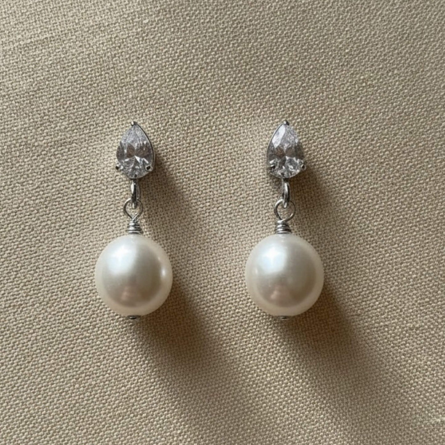 White pearl and crystal earrings resting on white satin, clean bright lighting, timeless bridal style