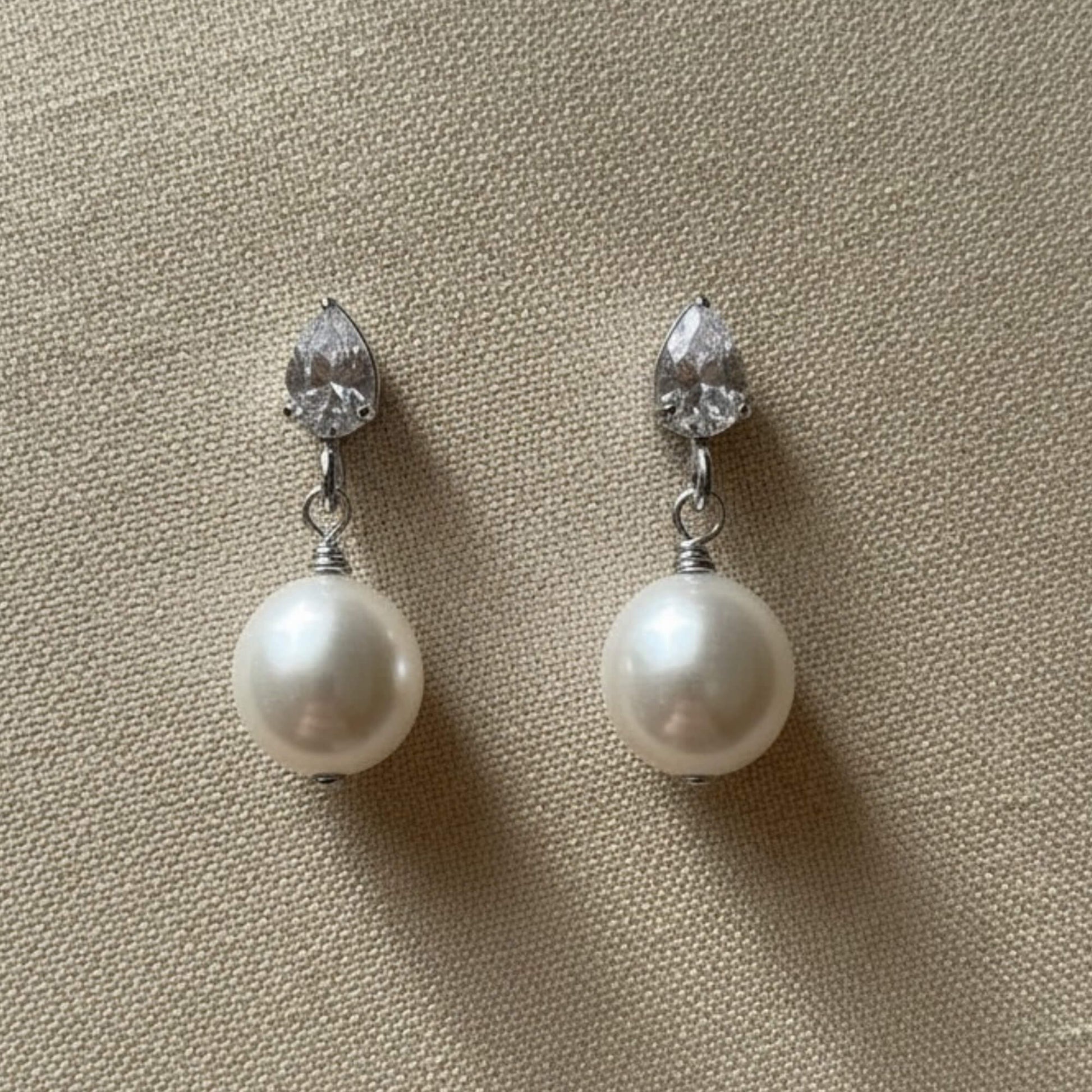 White pearl and crystal earrings resting on white satin, clean bright lighting, timeless bridal style