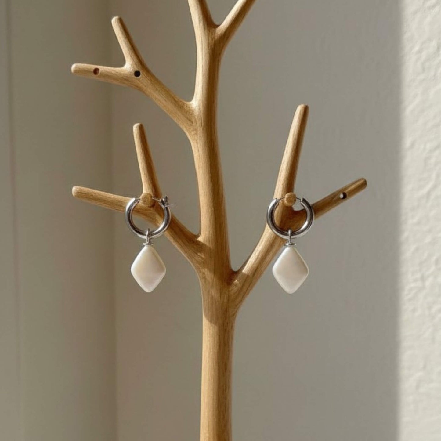 Silver hoop earrings featuring smooth ivory drop pendants displayed on soft white fabric, elegant product shot.