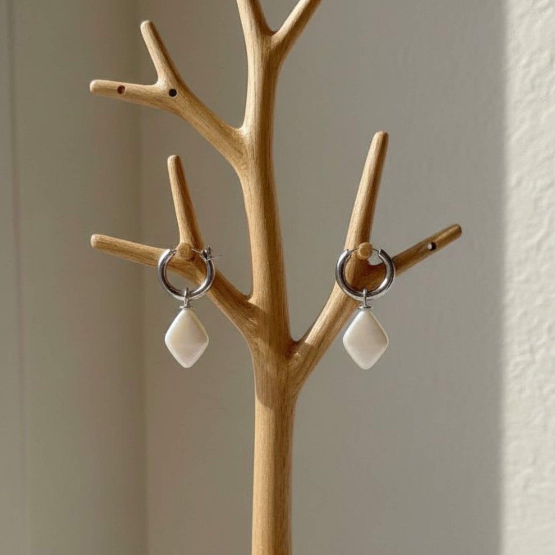 Silver hoop earrings featuring smooth ivory drop pendants displayed on soft white fabric, elegant product shot.