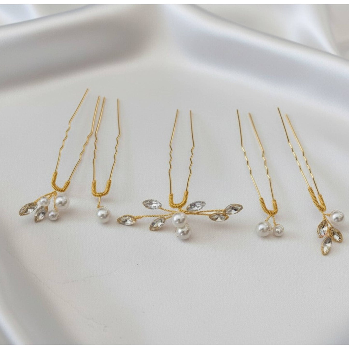 Set of 5 pearl and crystal bridal hair pins in gold displayed on white satin.