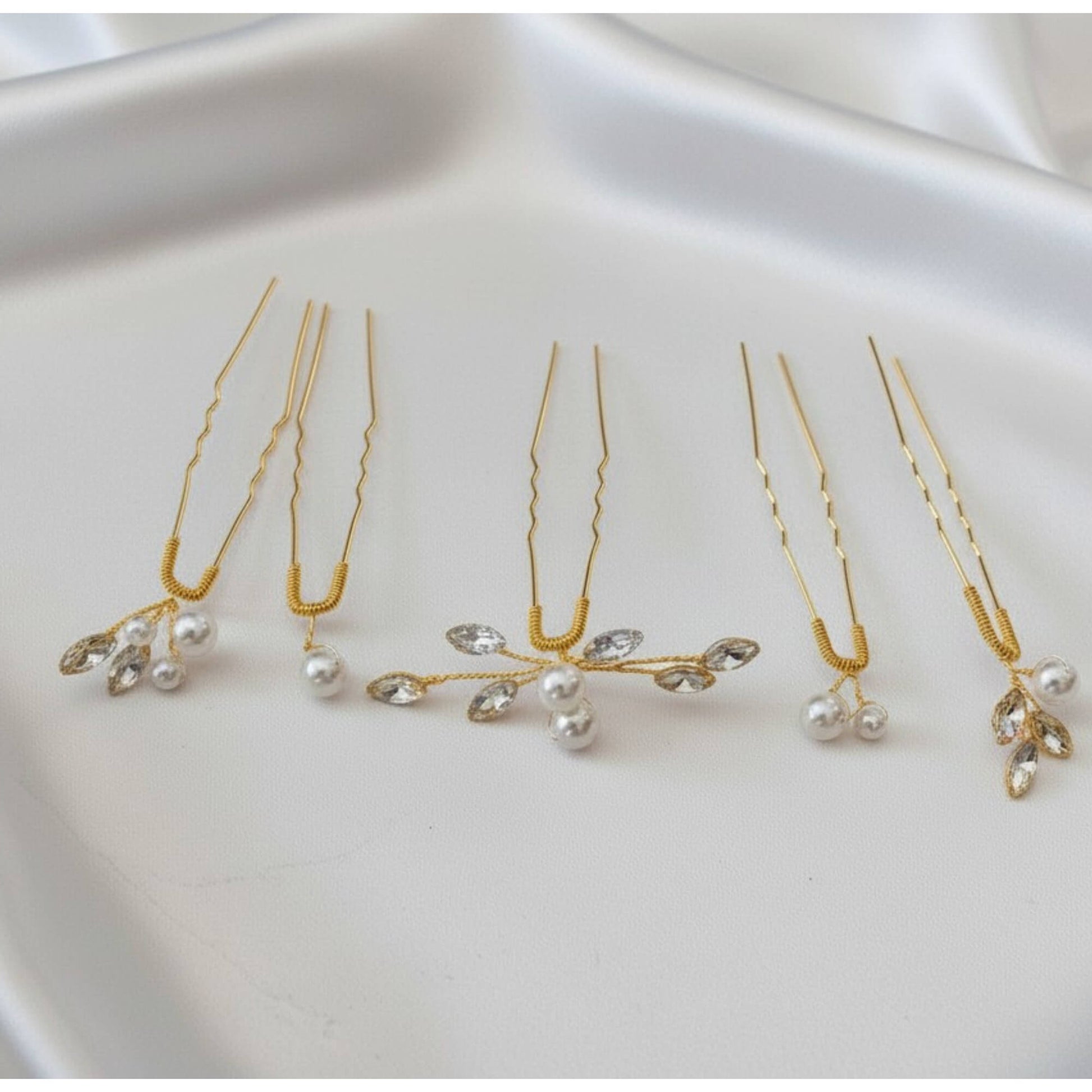 Set of 5 pearl and crystal bridal hair pins in gold displayed on white satin.