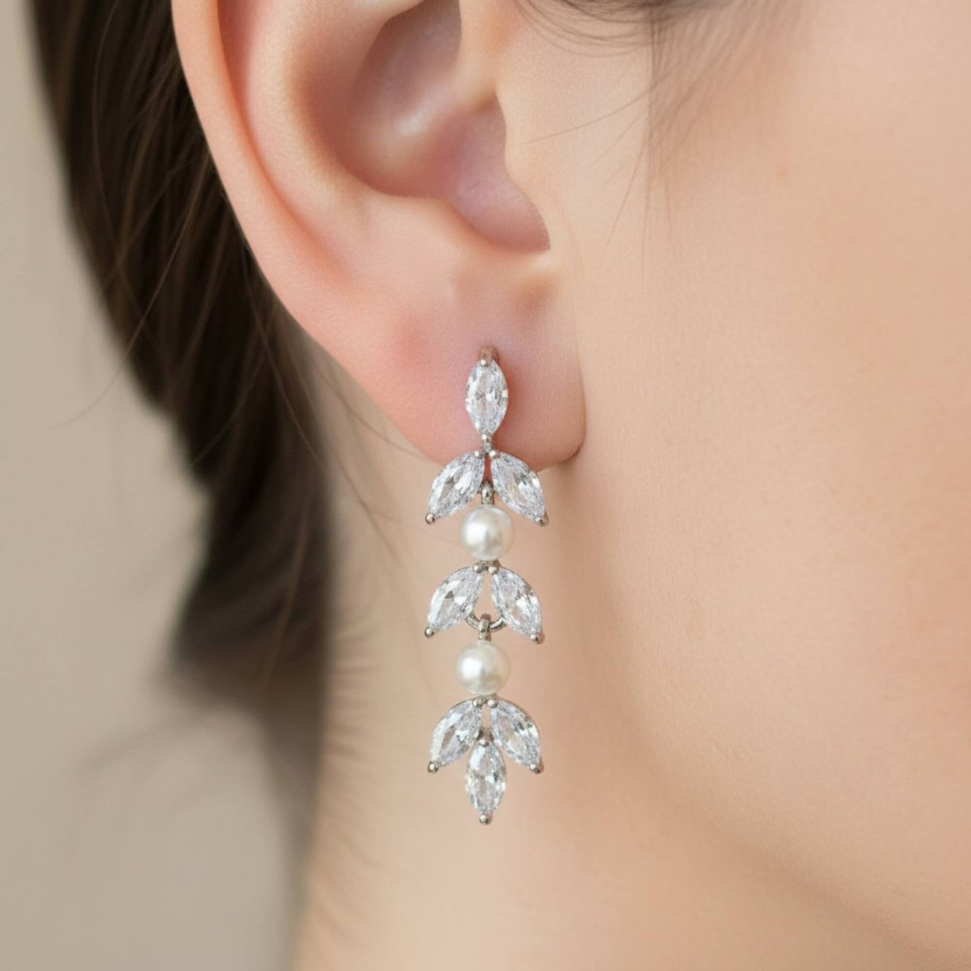 Bride wearing pearl and crystal drop earrings, close-up of ear and neckline in soft natural light.