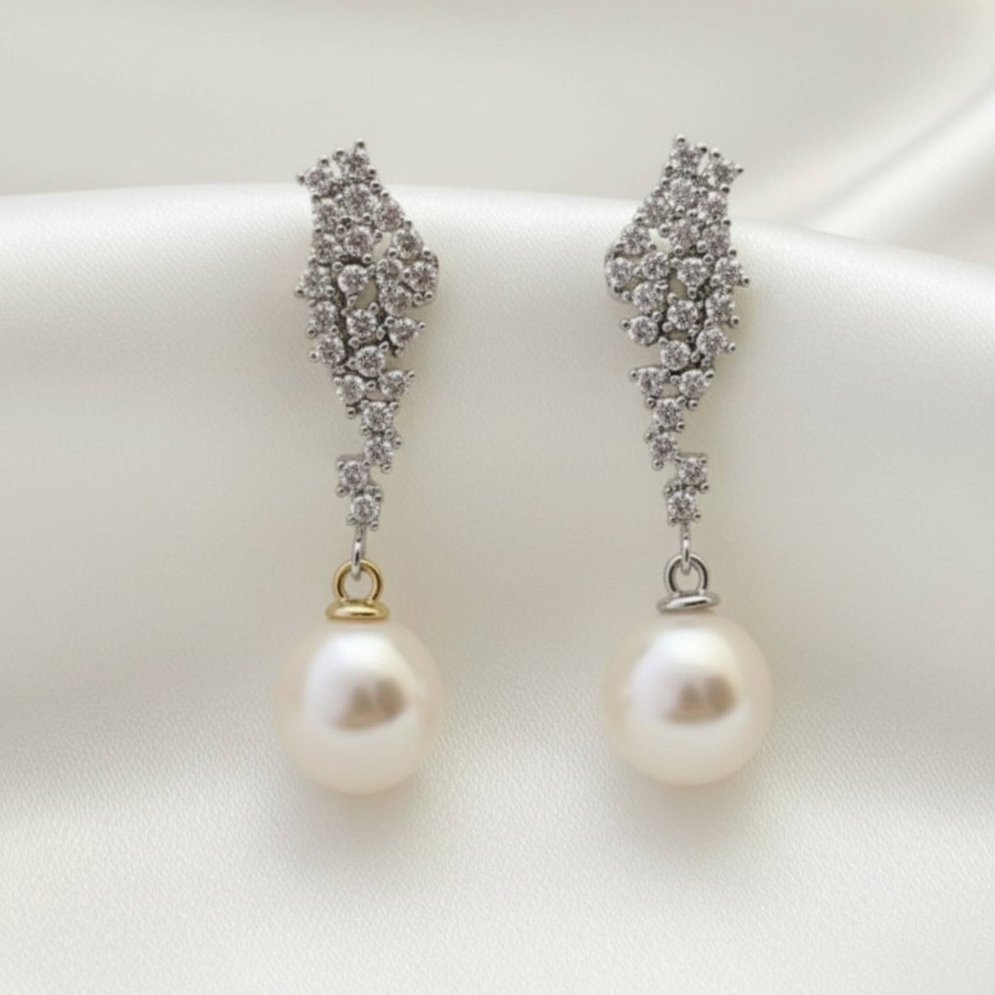 Close-up of gold crystal and pearl drop earrings on soft satin background, minimal premium bridal styling.