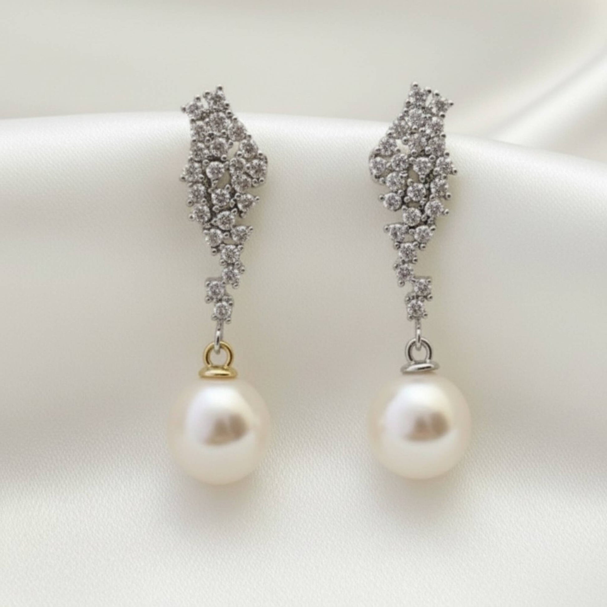 Close-up of gold crystal and pearl drop earrings on soft satin background, minimal premium bridal styling.
