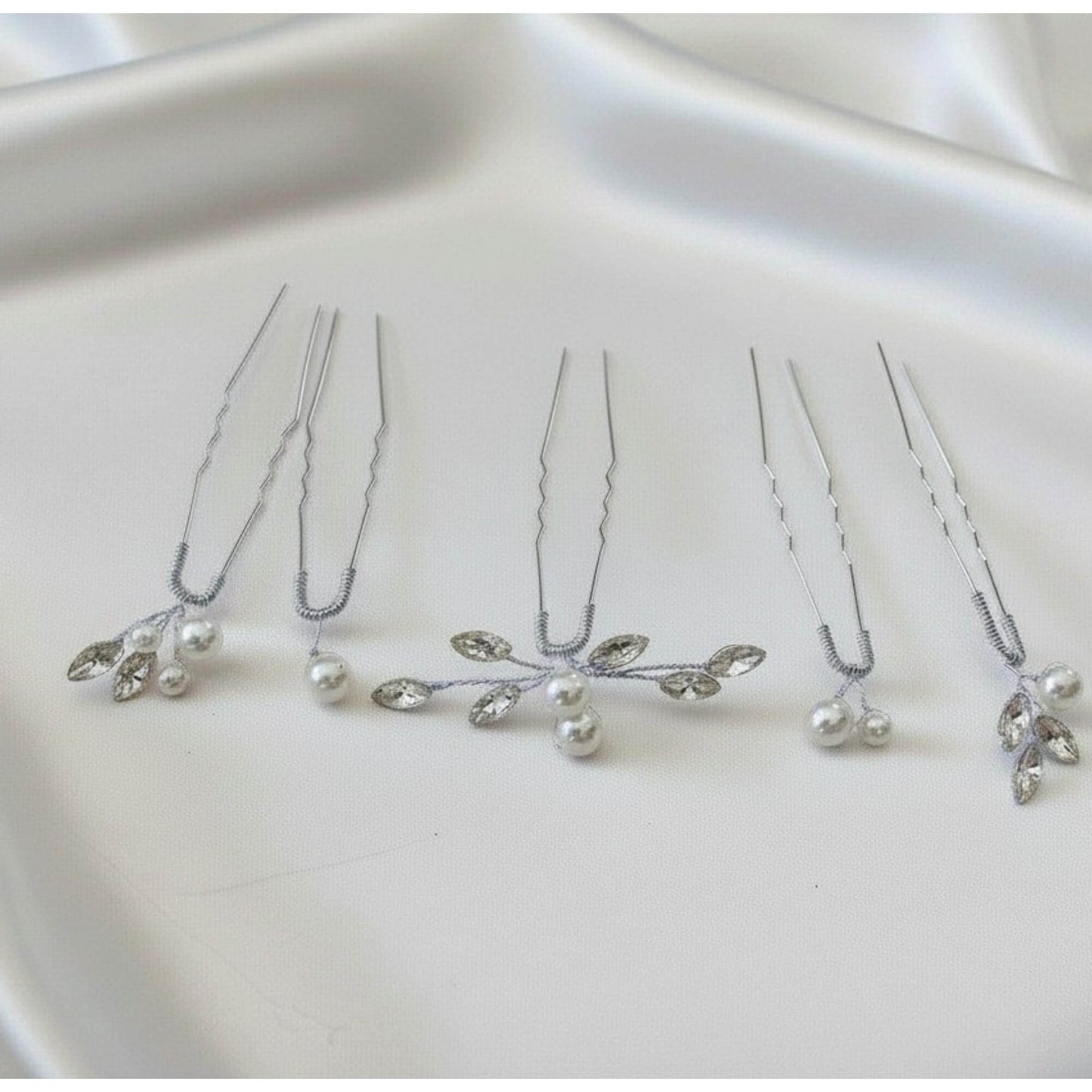Silver bridal hair pins with pearls and marquise crystals on a satin background.