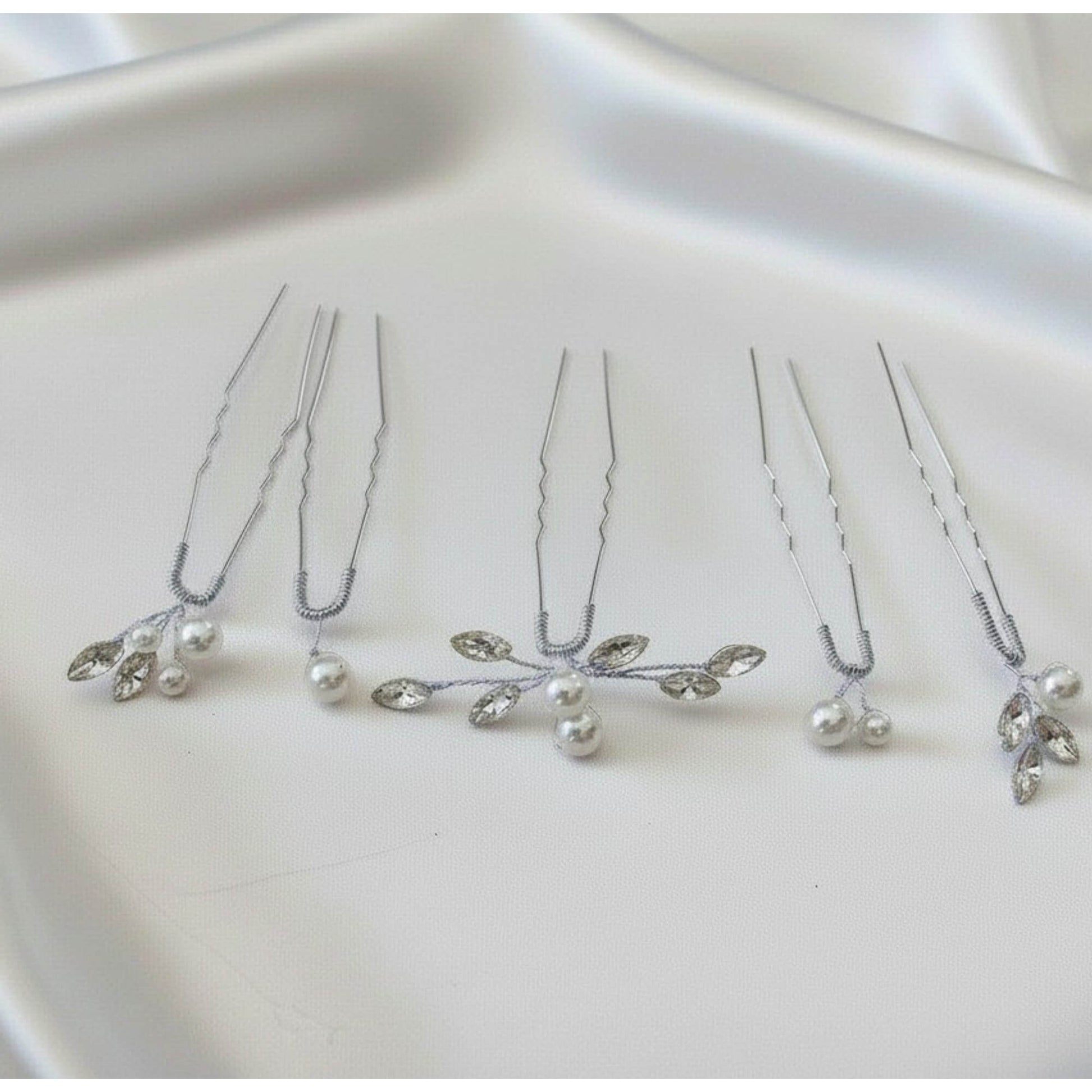 Silver bridal hair pins with pearls and marquise crystals on a satin background.