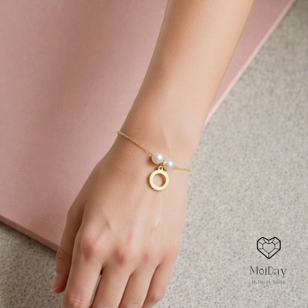 Gold bracelet with a pearl on a wrist against a neutral background, featuring the brand 'Moi Day'.