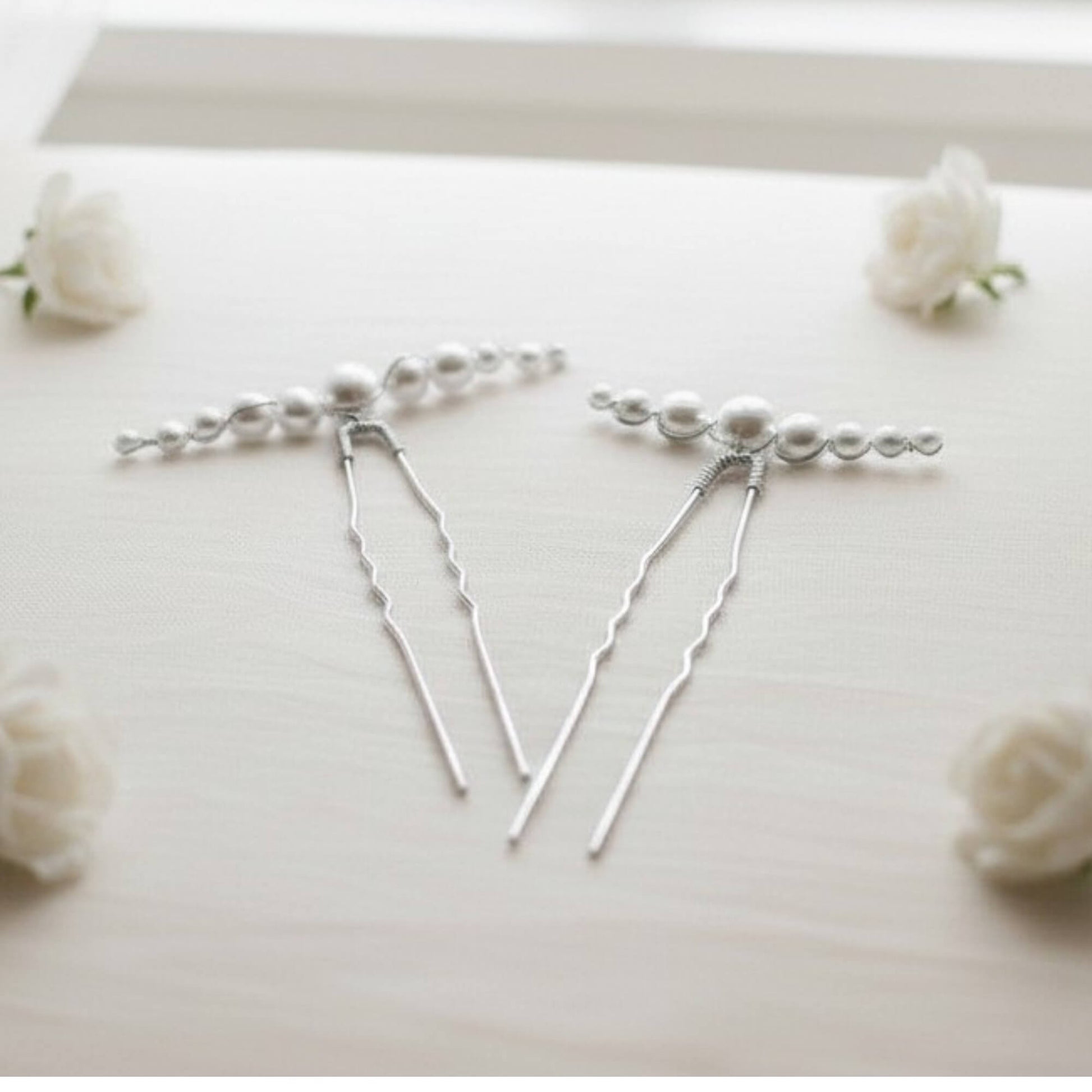 Silver hairpins with pearls on a white surface with small white flowers.