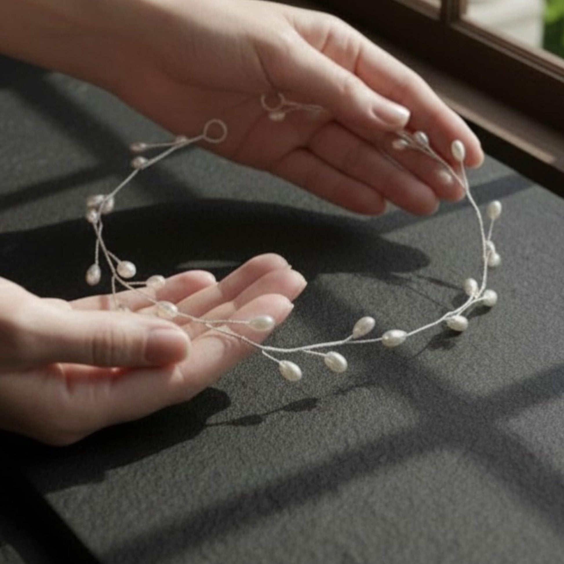 Hand holding a delicate floral hairpiece on a dark surface
