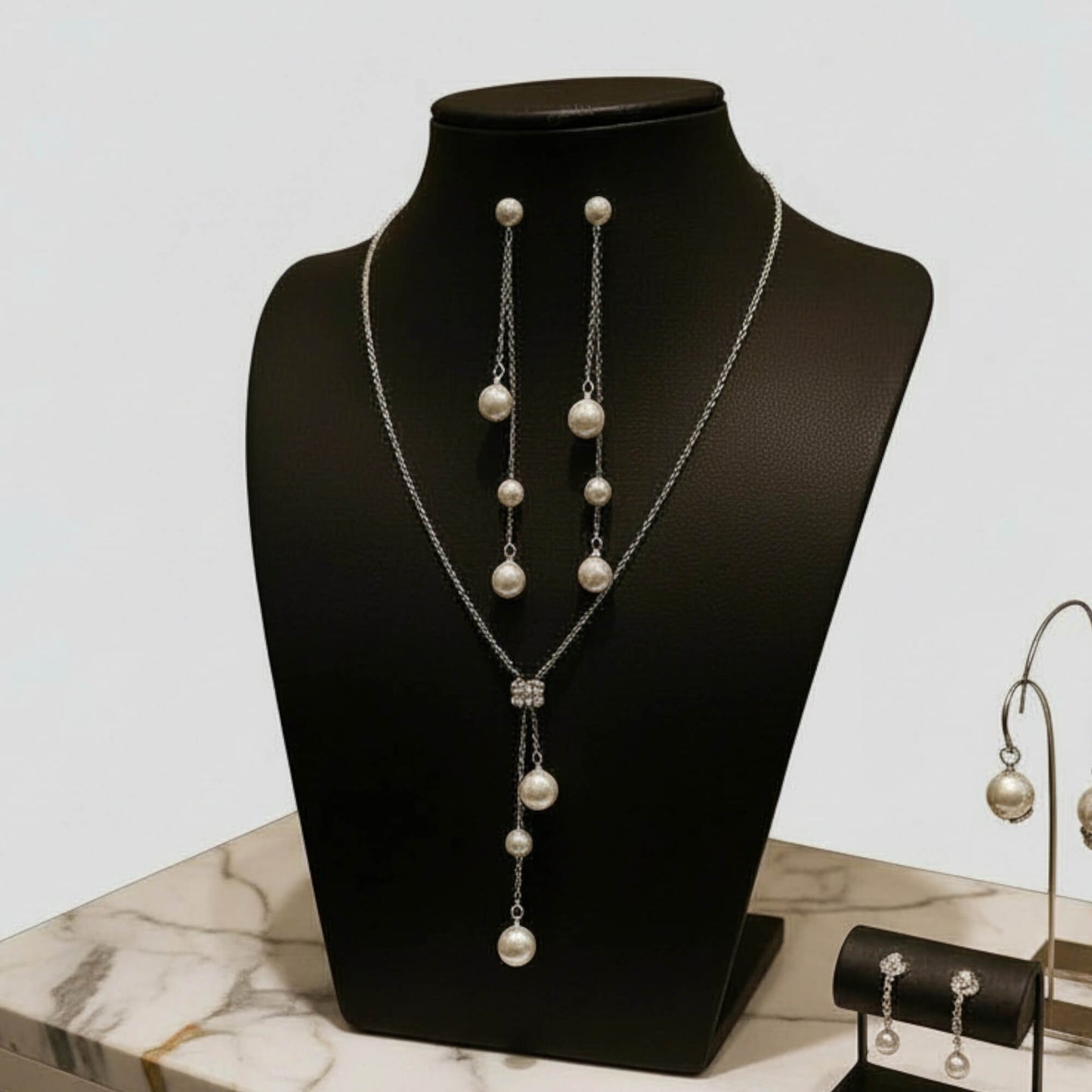 Pearl necklace and earrings set on a black mannequin bust with a marble surface.