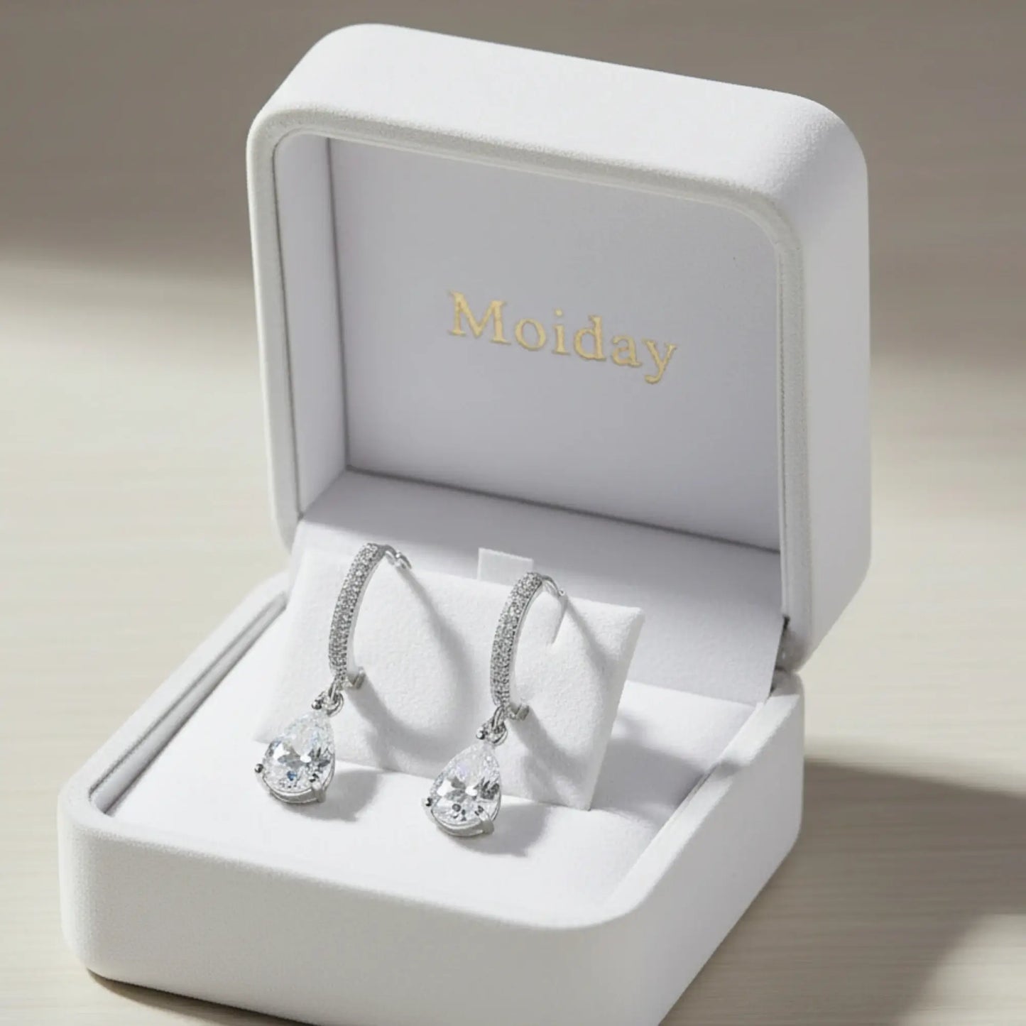 Silver earrings in a 'Moiday' jewelry box on a beige background