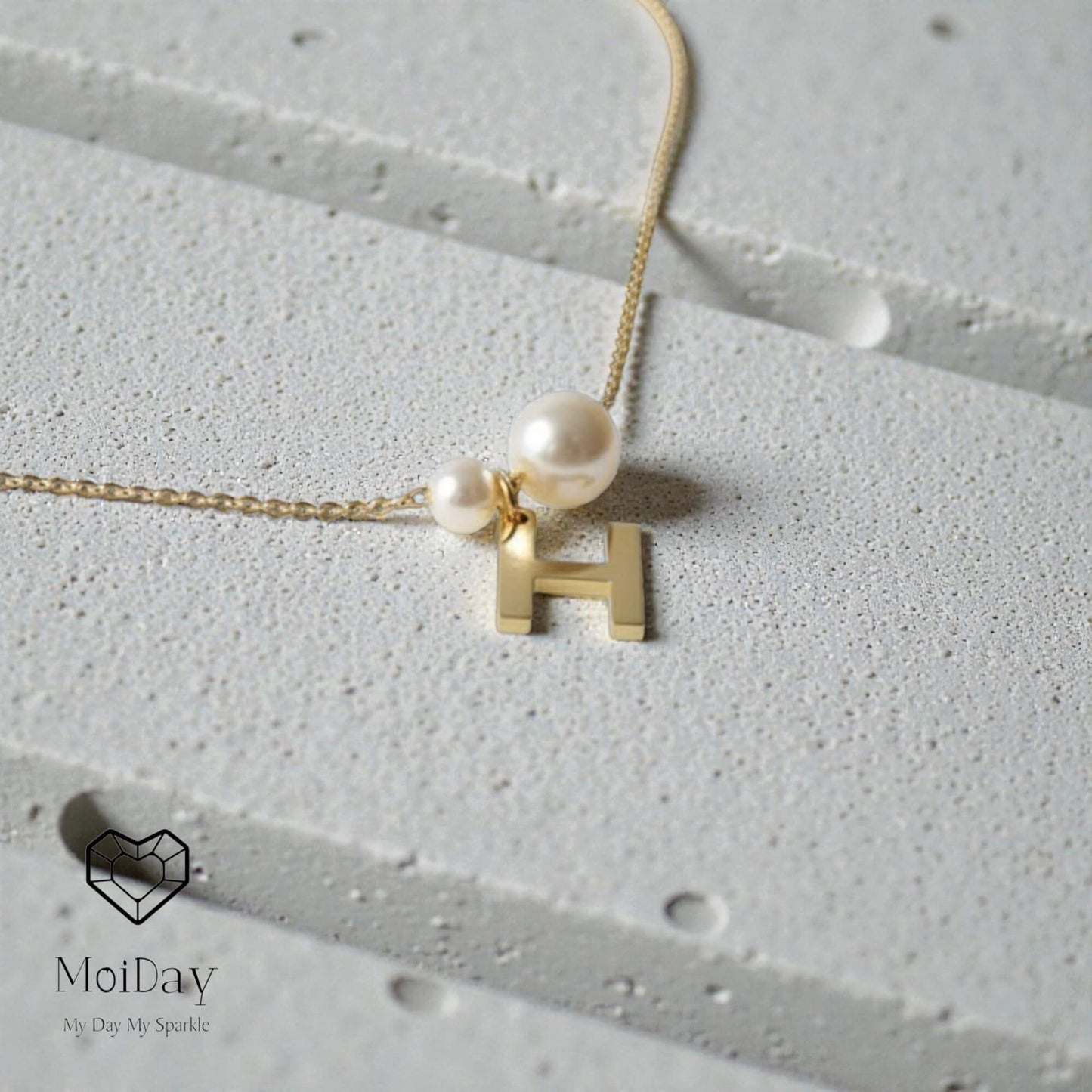 Necklace with pearl pendant and 'H' letter on a textured surface, MoiDay brand visible.