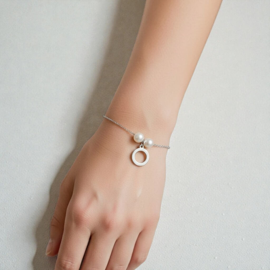 Silver bracelet with a circular charm and pearl on a wrist against a neutral background