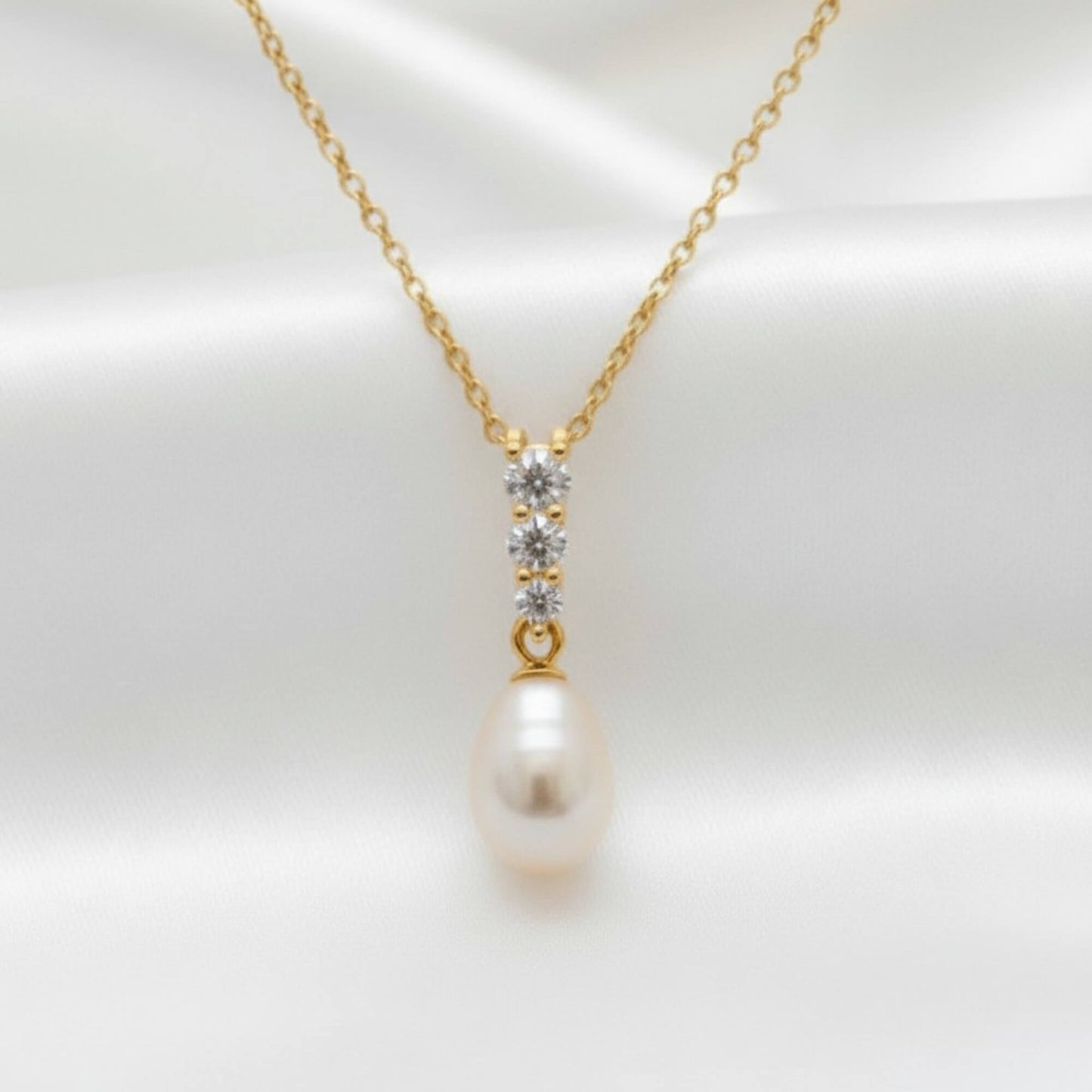 Close‑up of gold teardrop pearl necklace with crystal accents displayed on satin fabric, elegant bridal jewellery Australia.