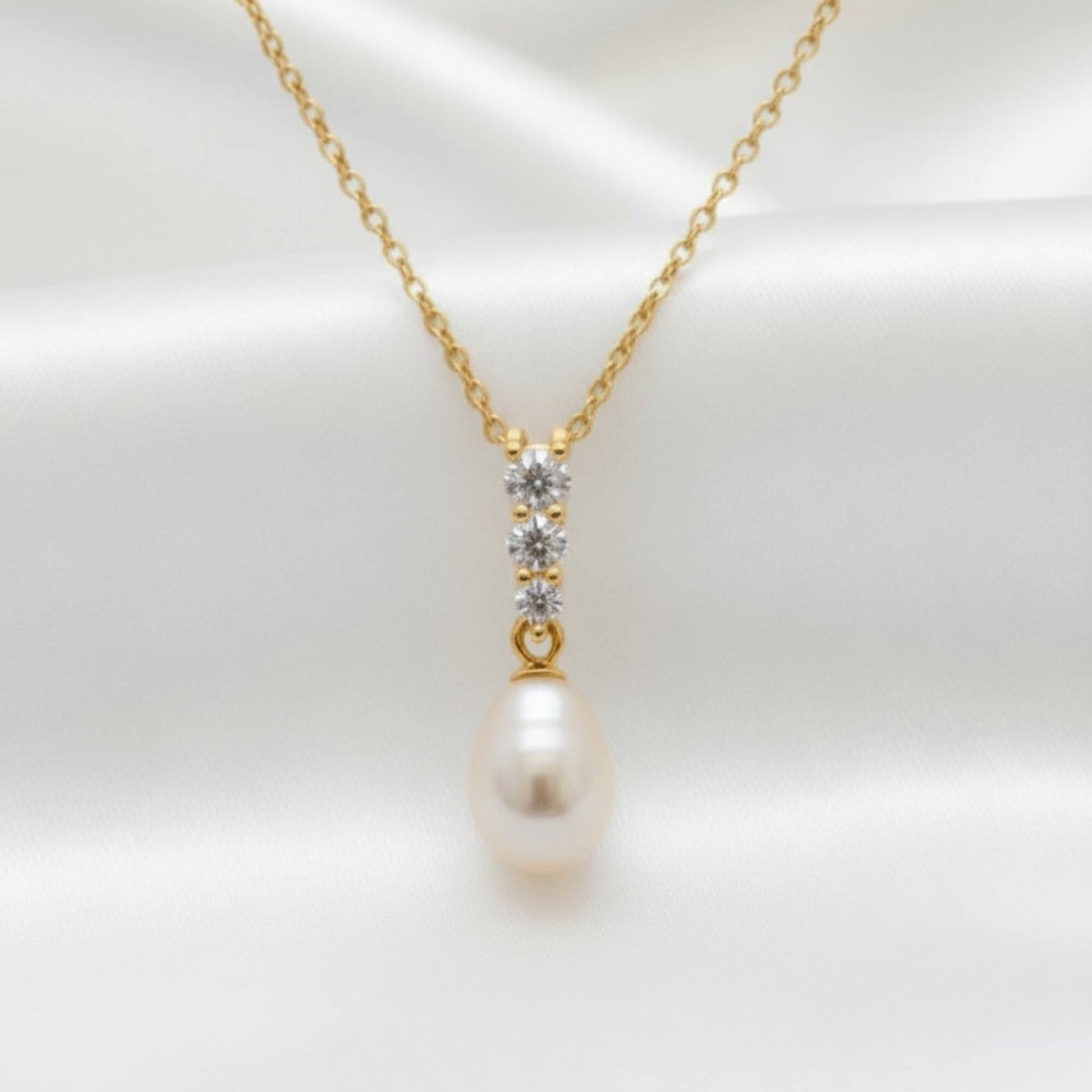 Close‑up of gold teardrop pearl necklace with crystal accents displayed on satin fabric, elegant bridal jewellery Australia.