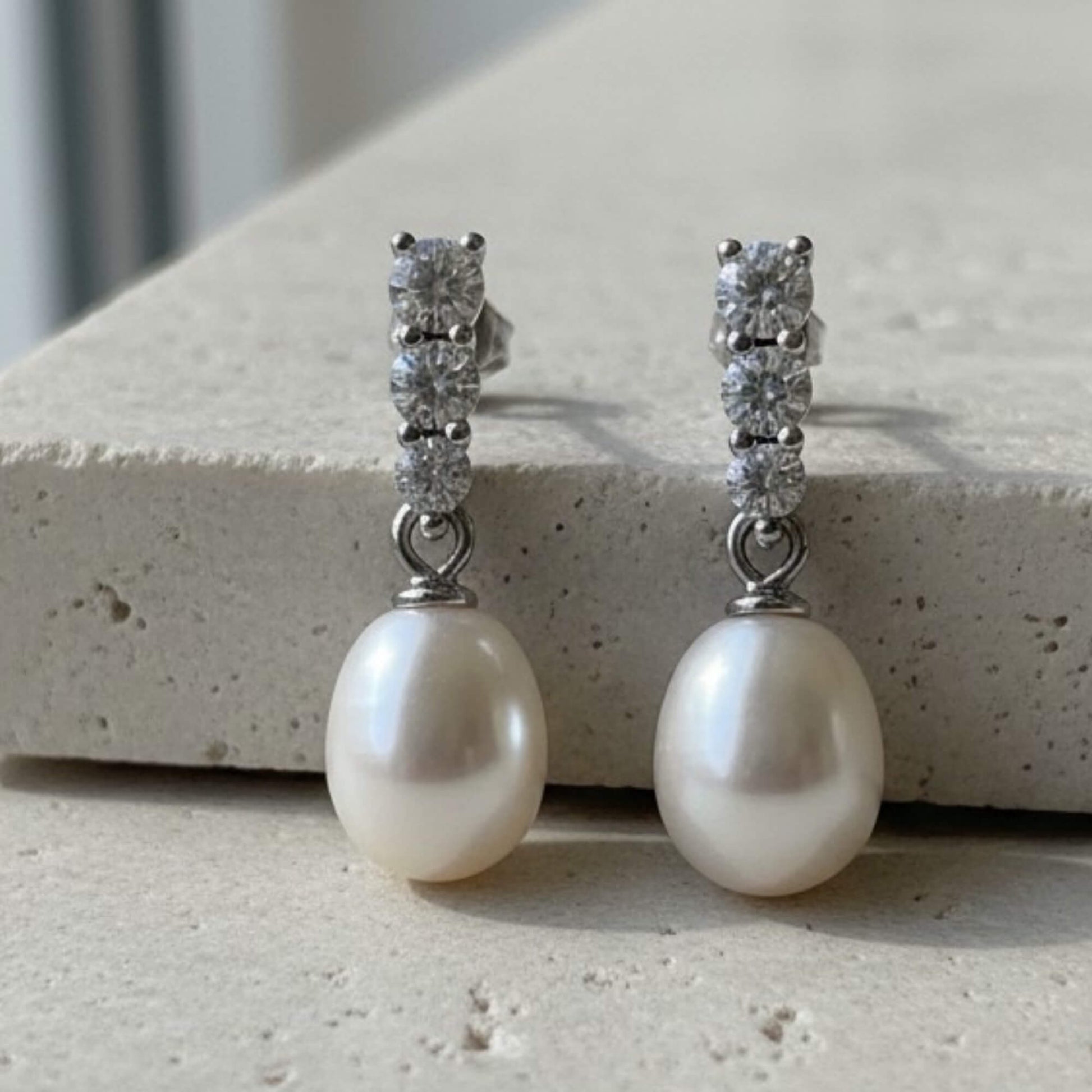 Pearl earrings with diamond-like stones on a stone surface