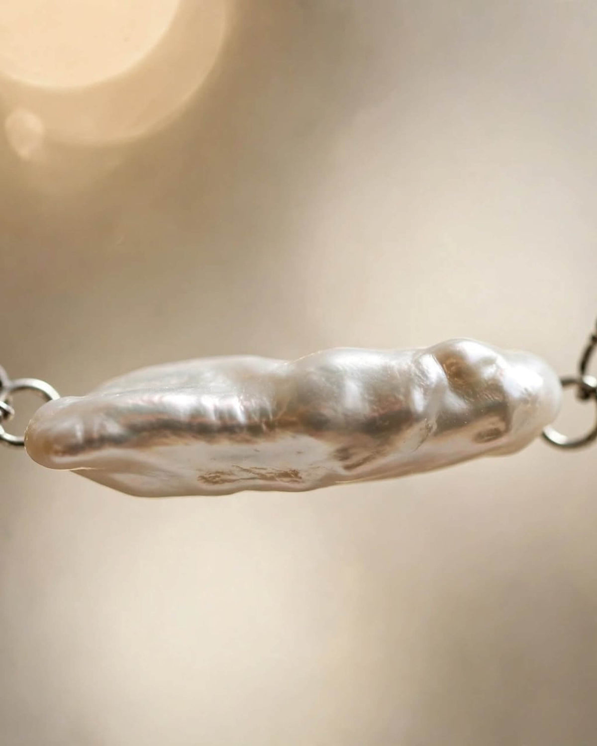 A close-up of a silver-toned chain bracelet featuring a large, irregular baroque pearl pendant with a polished, lustrous finish.