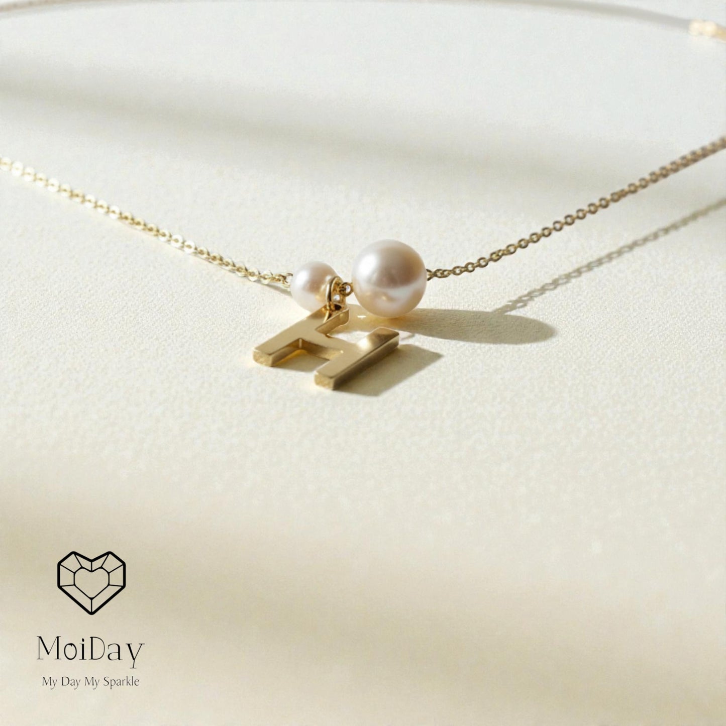 Gold necklace with a pearl pendant on a light beige background, featuring the brand 'MoiDay'.