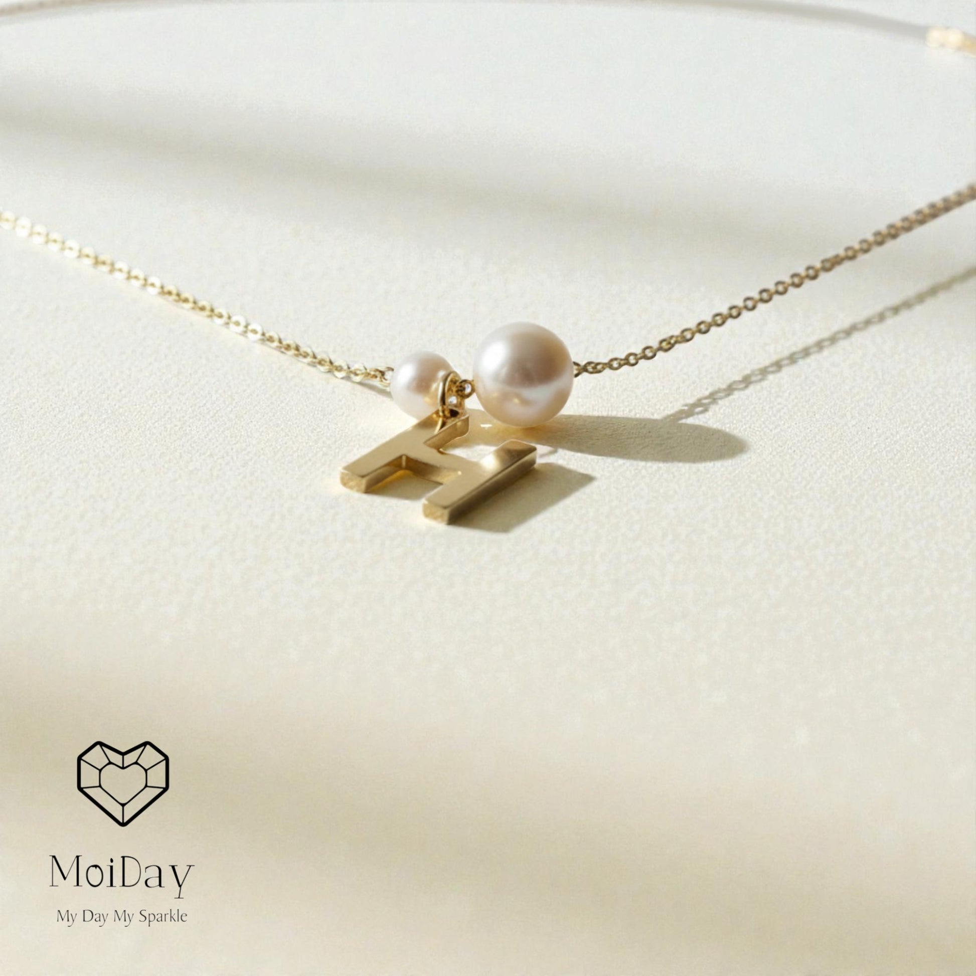Gold necklace with a pearl pendant on a light beige background, featuring the brand 'MoiDay'.